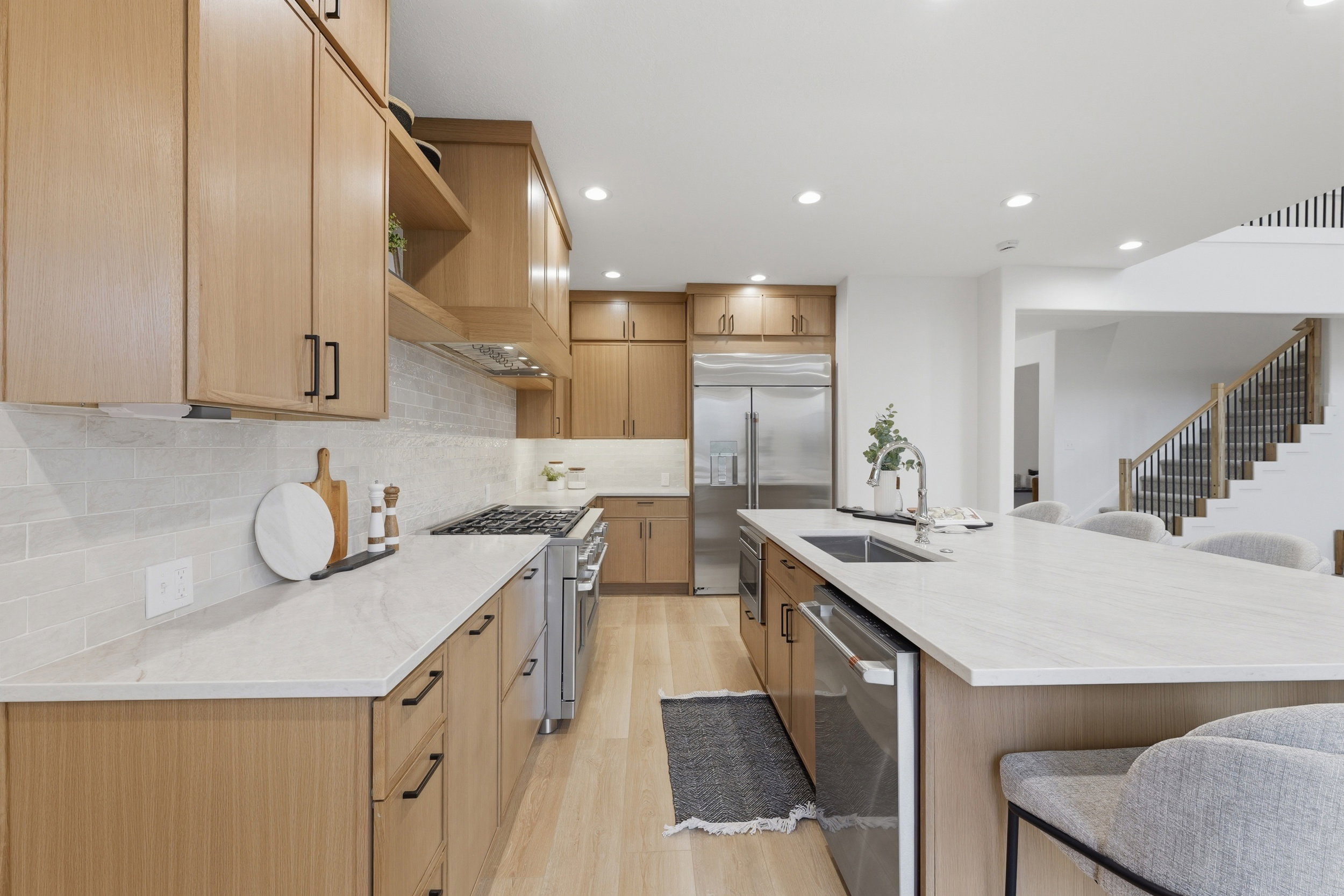 Contemporary kitchen featuring light wood-finish cabinetry, quartz countertops, a subway tile backsplash, stainless steel appliances, and wood-finish flooring