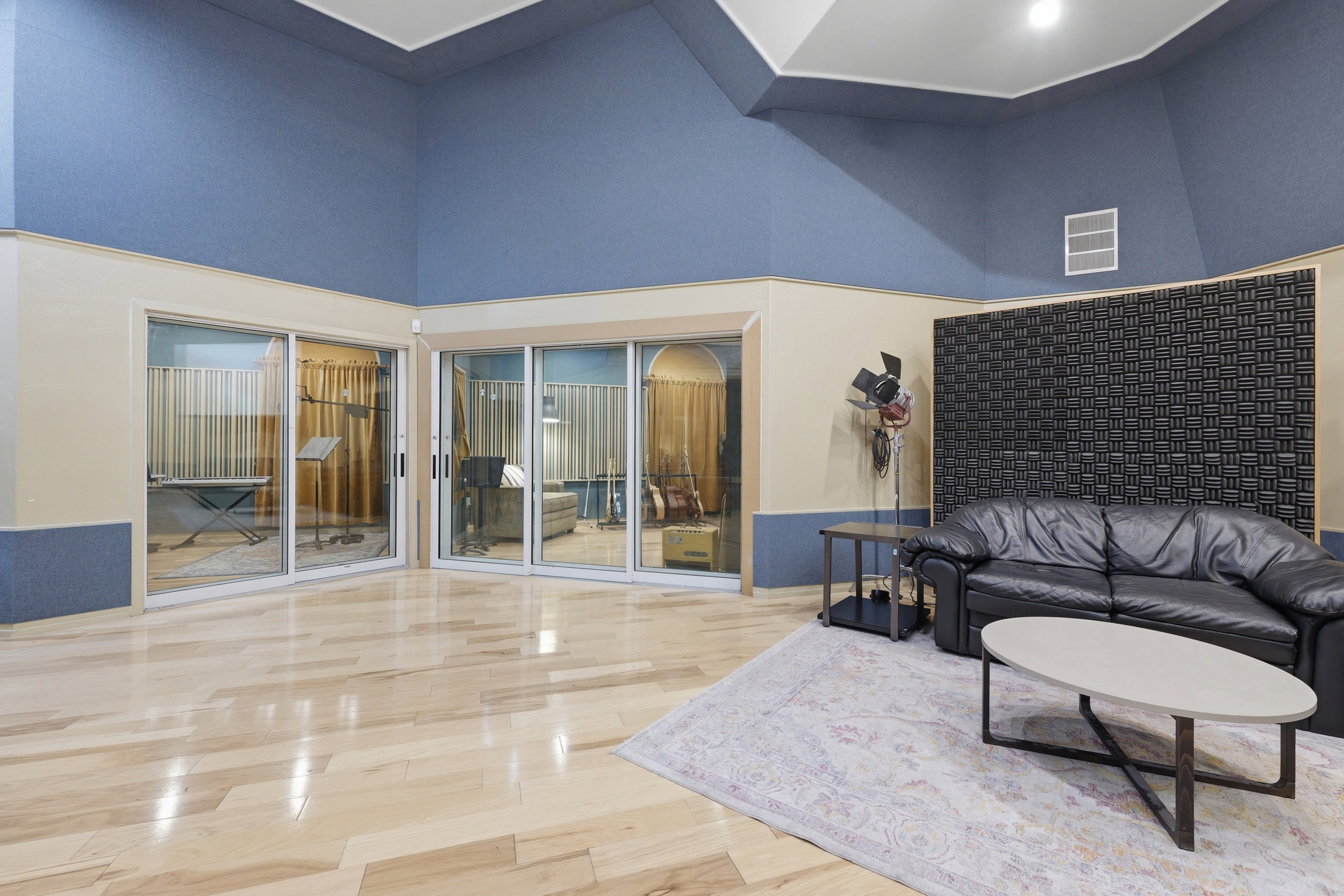 Professional recording studio featuring light wood-finish flooring, sound-absorbing wall panels, and multiple soundproofed rooms with sliding glass doors
