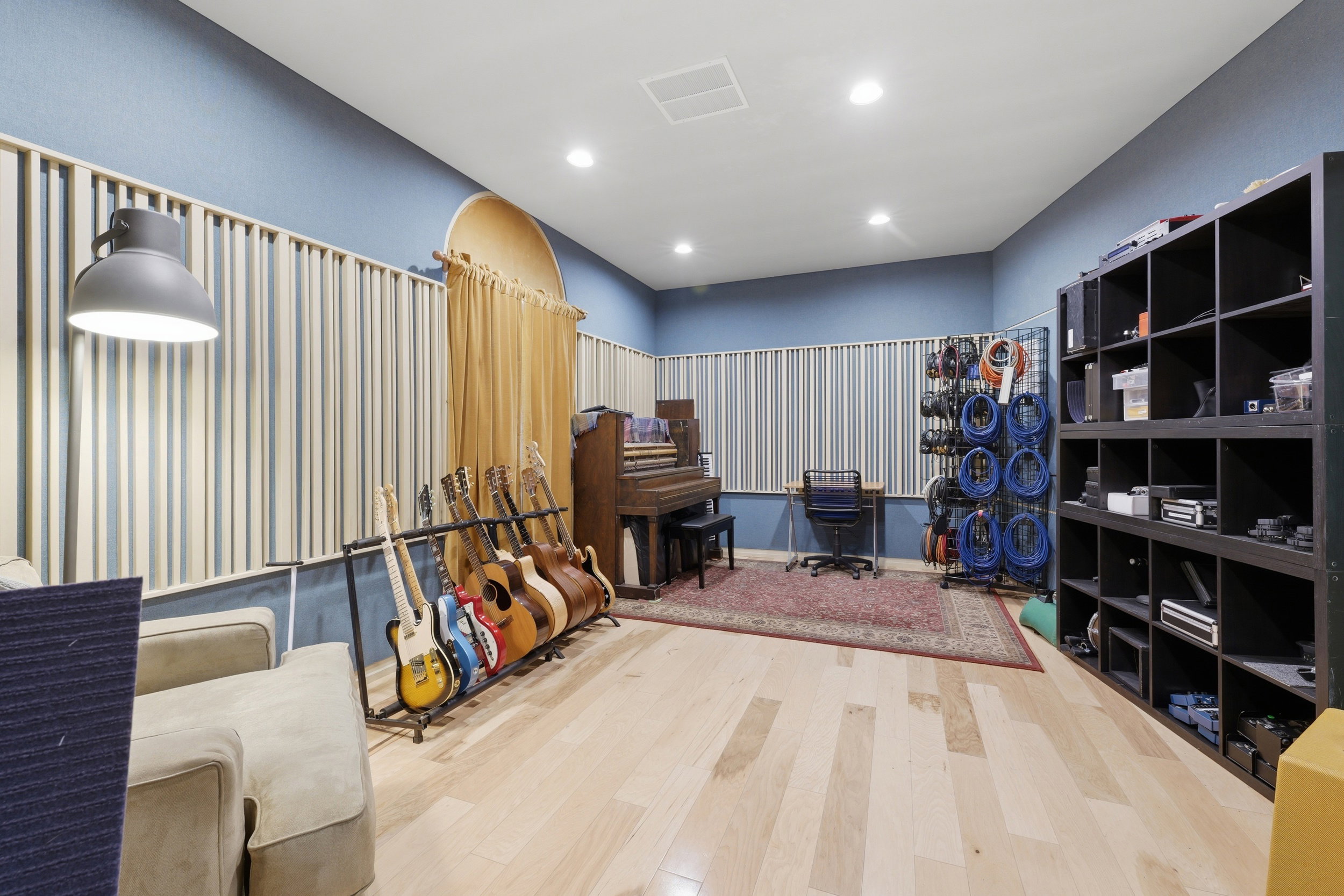 Recessed lighting illuminates a room featuring horizontal acoustic paneling, light wood-finish flooring, and a built-in shelving unit