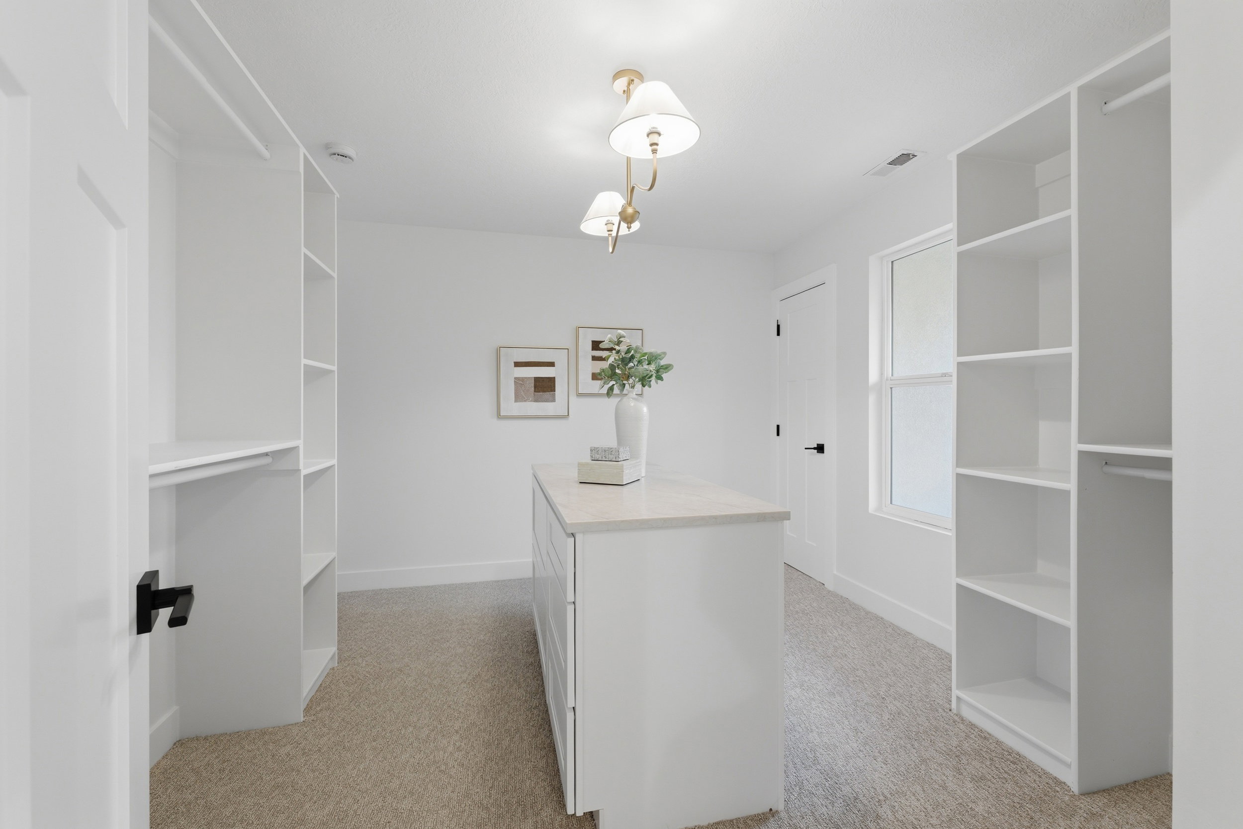 Spacious custom closet featuring a central island with a light-toned countertop, extensive built-in shelving, hanging rods, and a window providing natural light