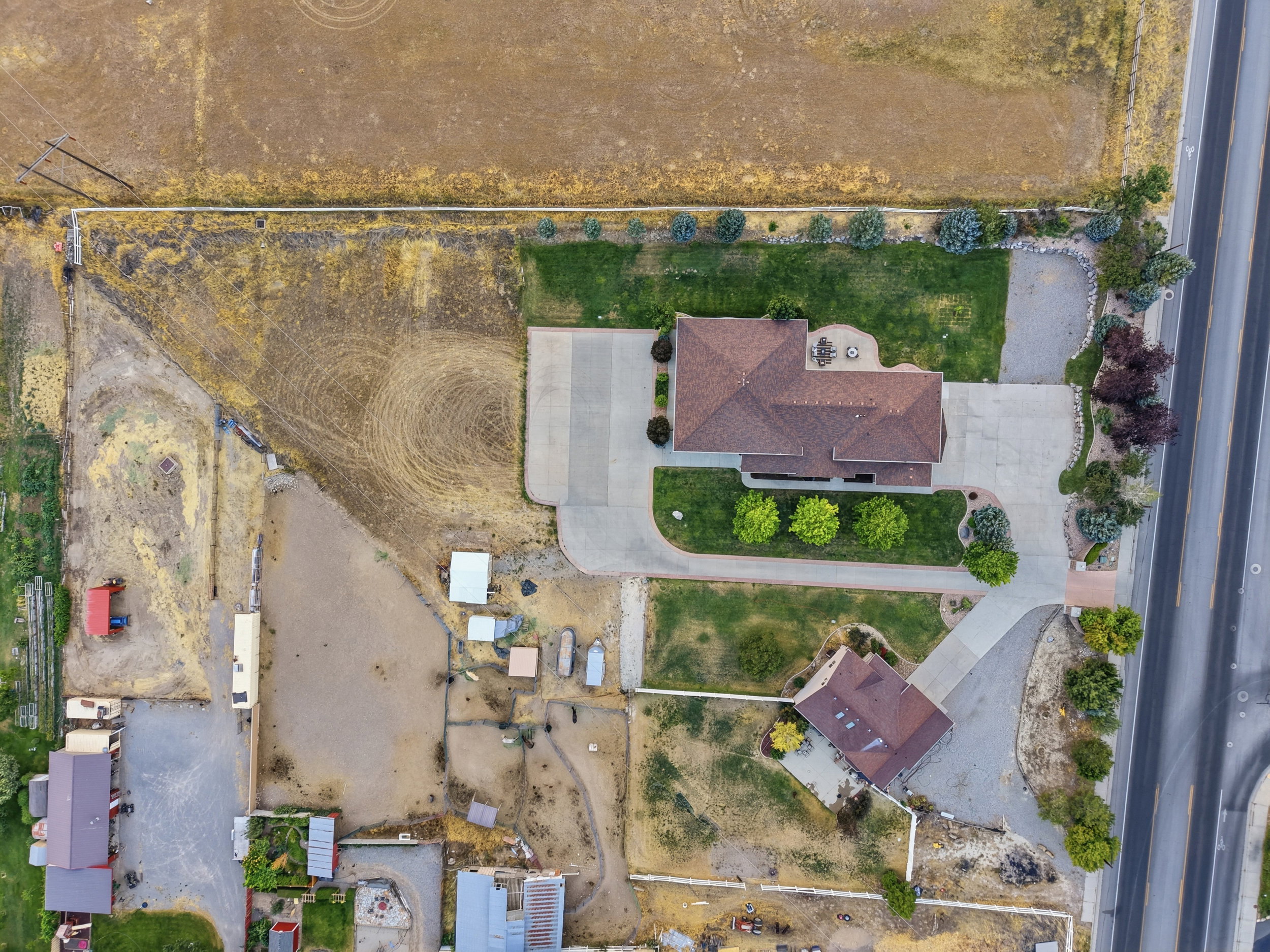 Expansive property featuring two distinct structures with complementary roofing, surrounded by varied landscaping, and direct road access