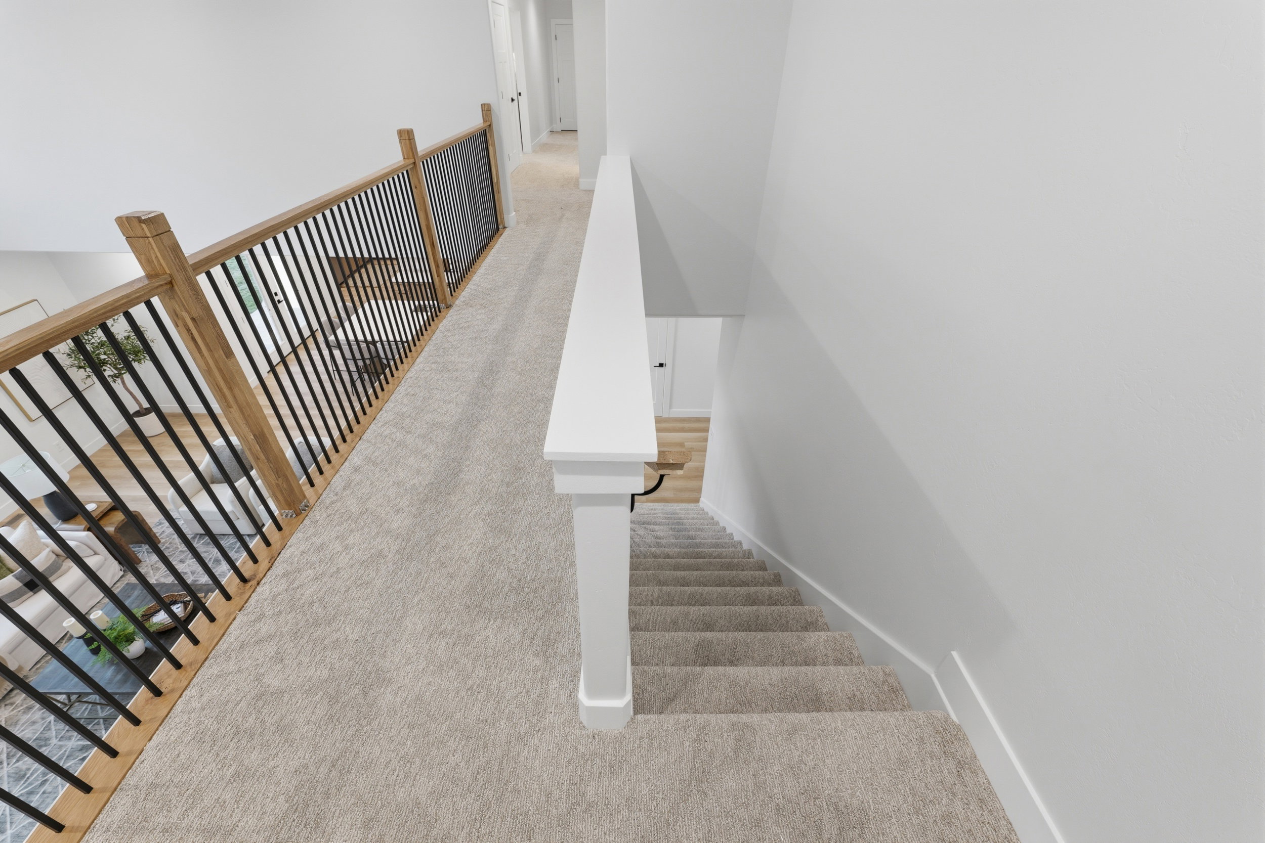 Upper-level hallway featuring light-toned carpeting, a white handrail, and a contemporary wood and black metal baluster system overlooking the lower level