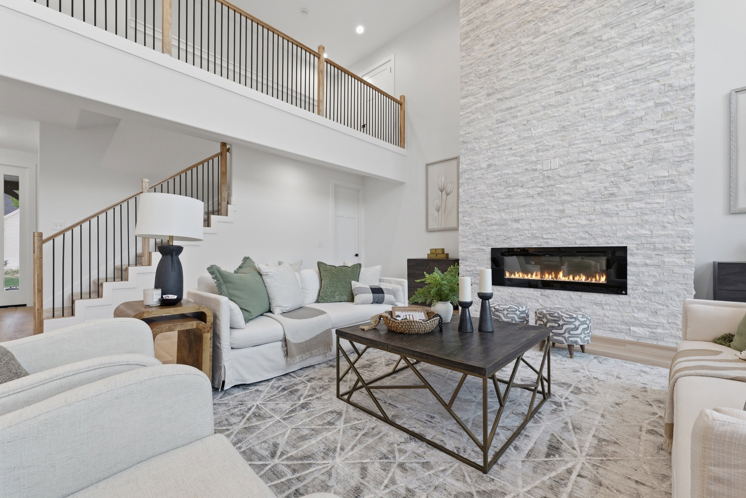 Two-story living area featuring a stacked stone fireplace with a linear insert, a grand staircase with wood newel posts and black metal balusters, and a second-story overlook