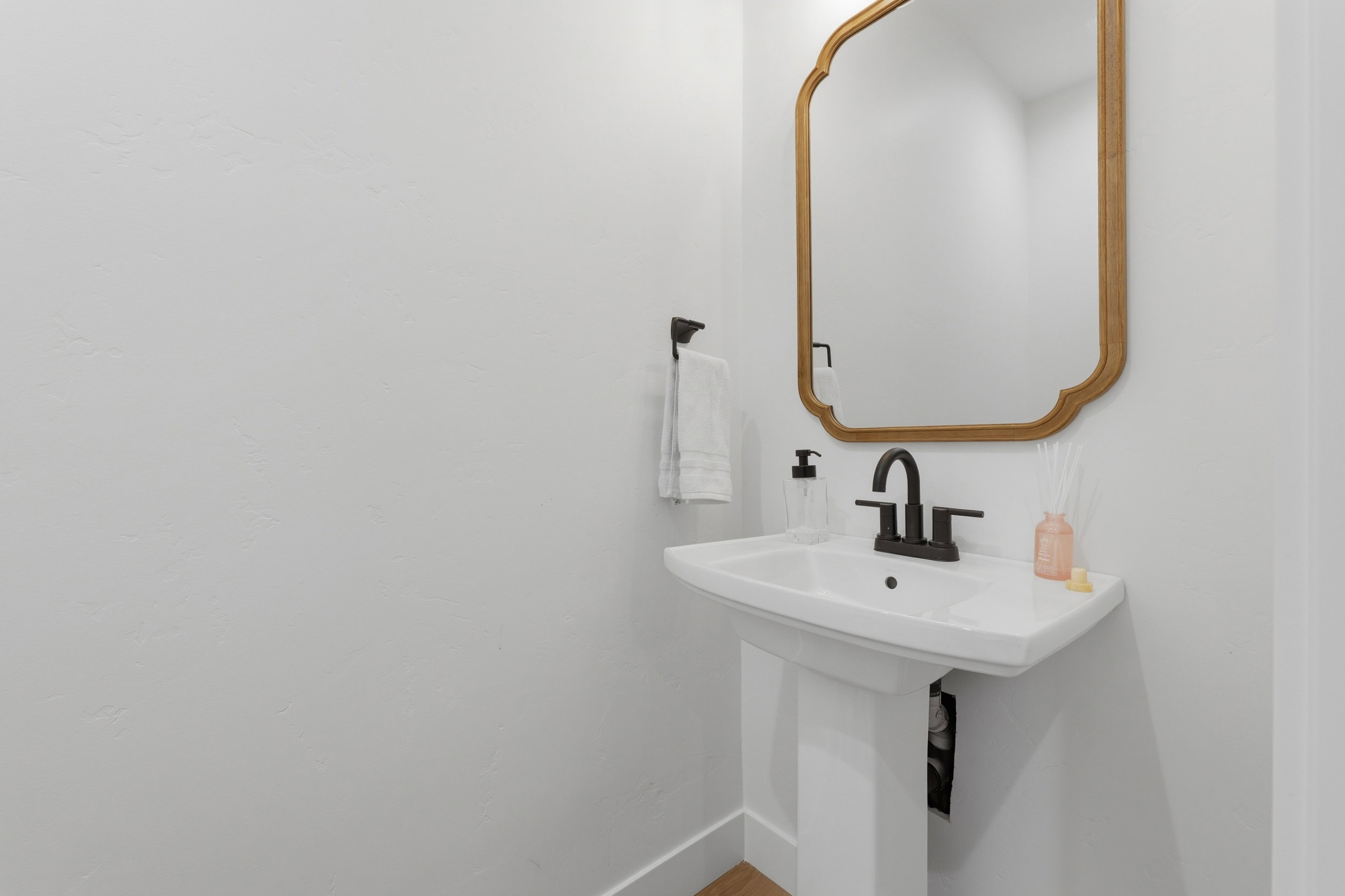 Pedestal sink with matte black faucet, framed by a decorative mirror