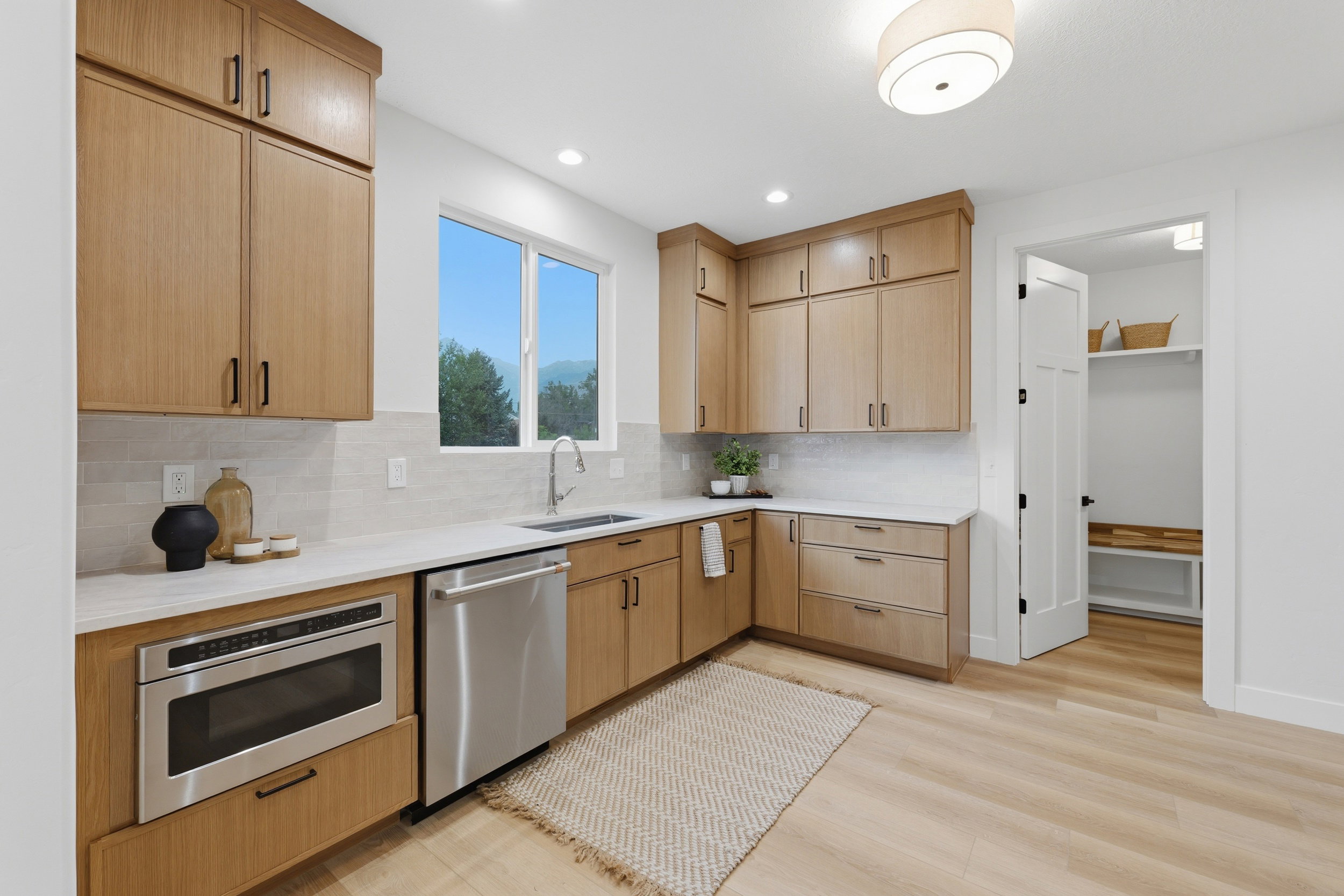Modern kitchen featuring light wood-finish cabinetry, stainless steel appliances, white countertops, and a full-height tile backsplash
