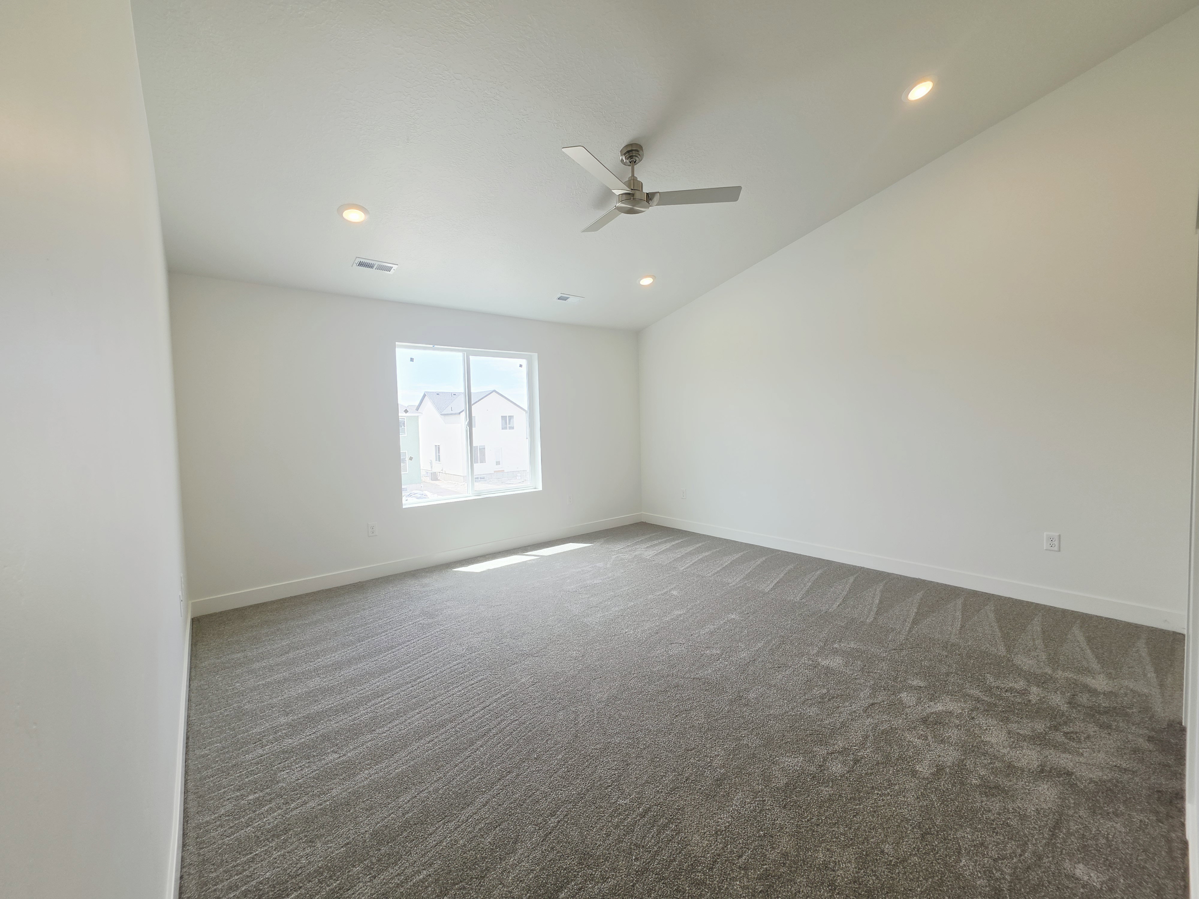 Spacious room featuring white walls, gray patterned carpet, a single window, and a ceiling fan with recessed lighting