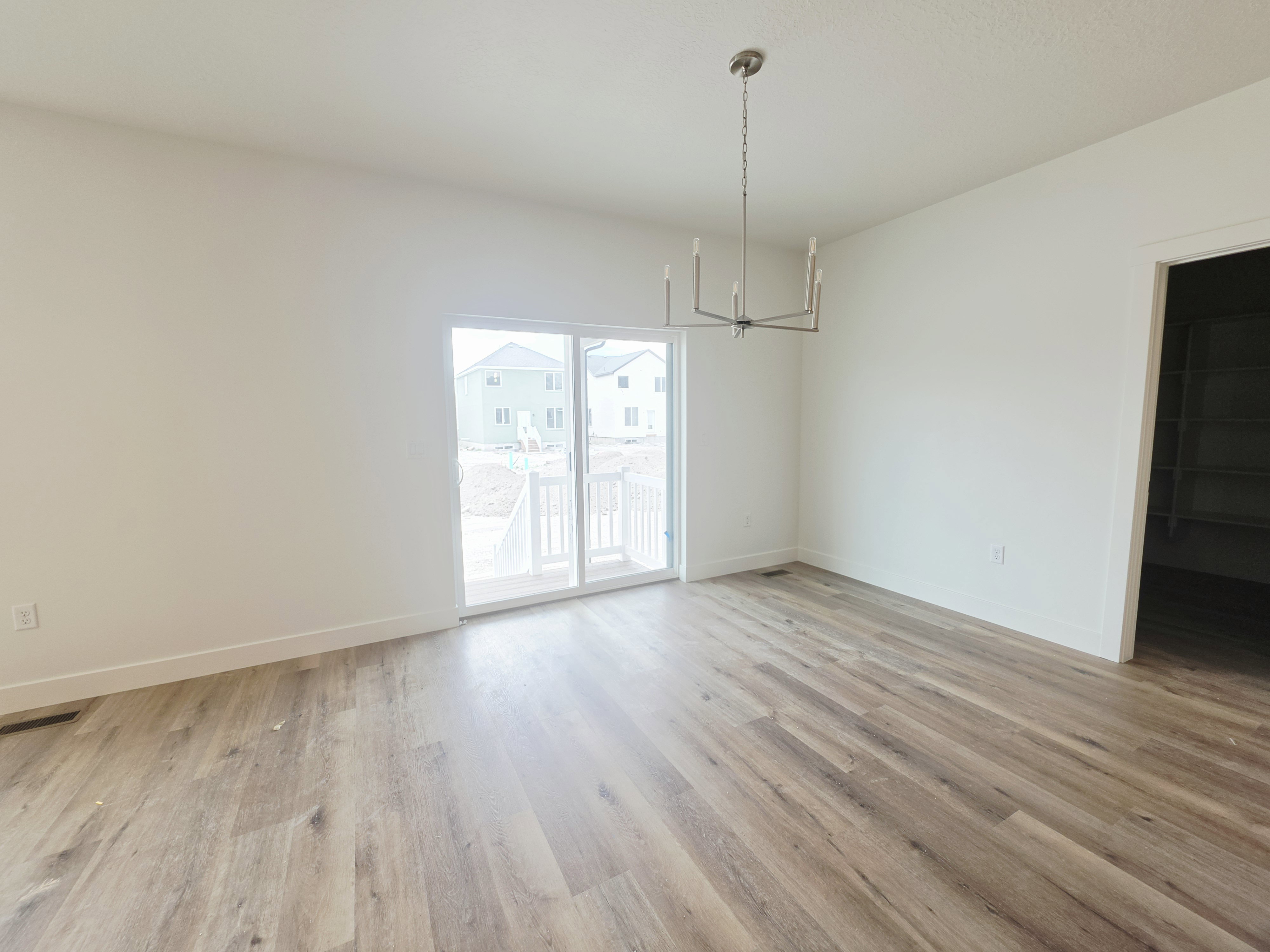 Spacious room featuring wood-finish flooring, a modern chandelier, and a sliding glass door leading to an outdoor deck with white railings