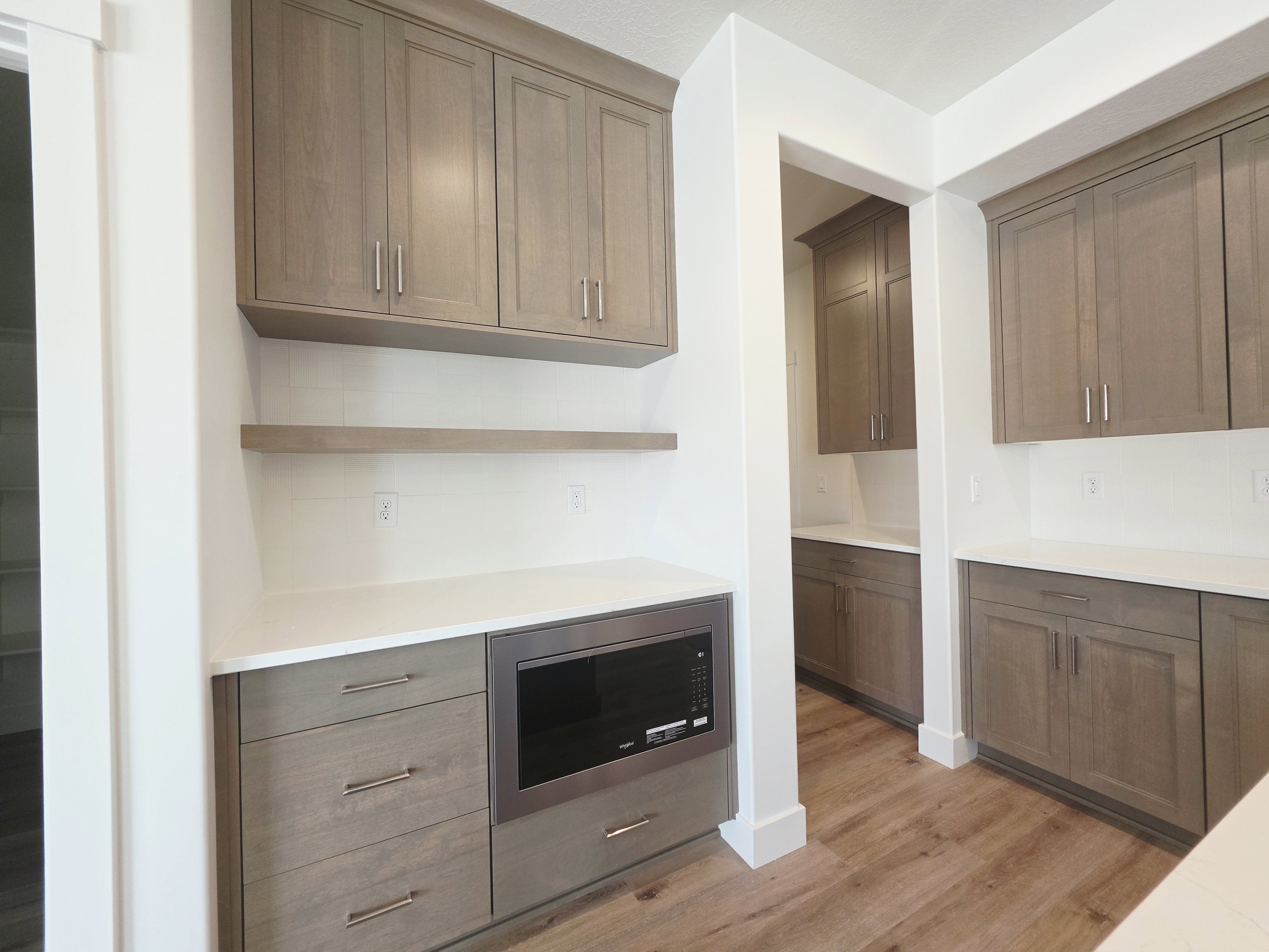 Custom cabinetry with brushed nickel hardware, built-in microwave, white countertops, wood-finish flooring, and white subway tile backsplash