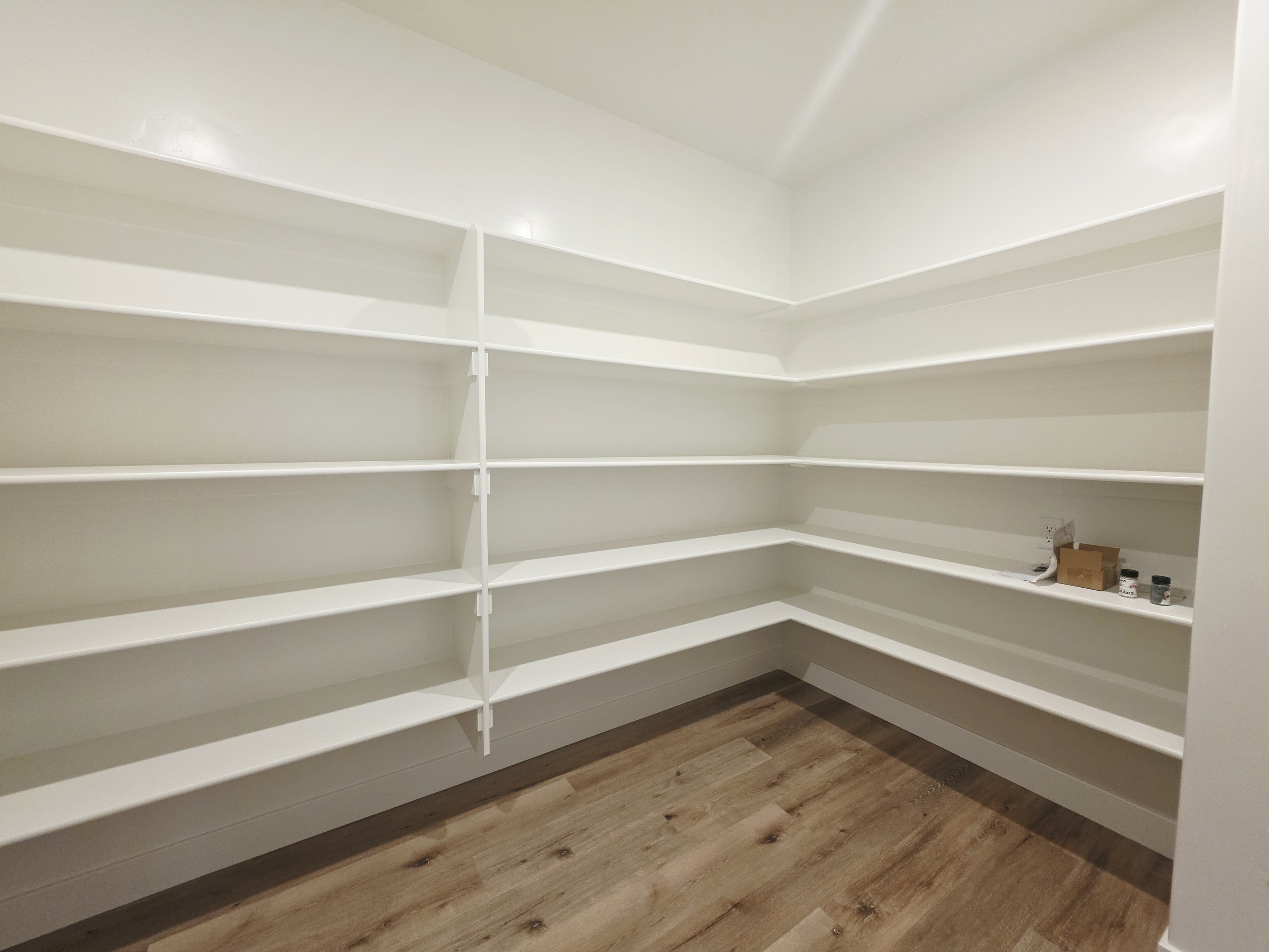 Dedicated pantry space featuring extensive built-in shelving, durable wood-finish flooring, and crisp white walls