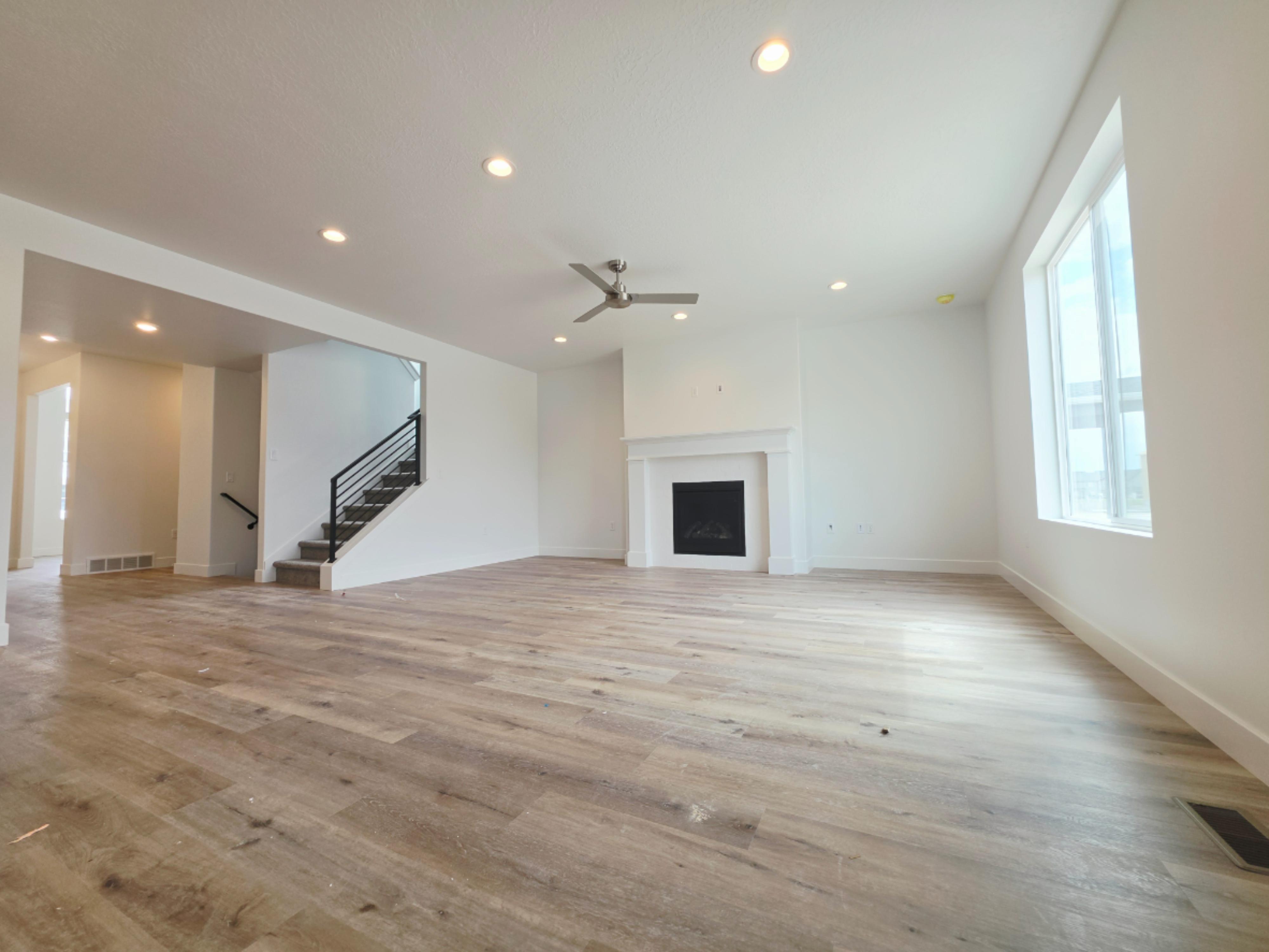 Spacious living area featuring wood-finish flooring, a contemporary fireplace with a white mantel, recessed lighting, and a modern ceiling fan