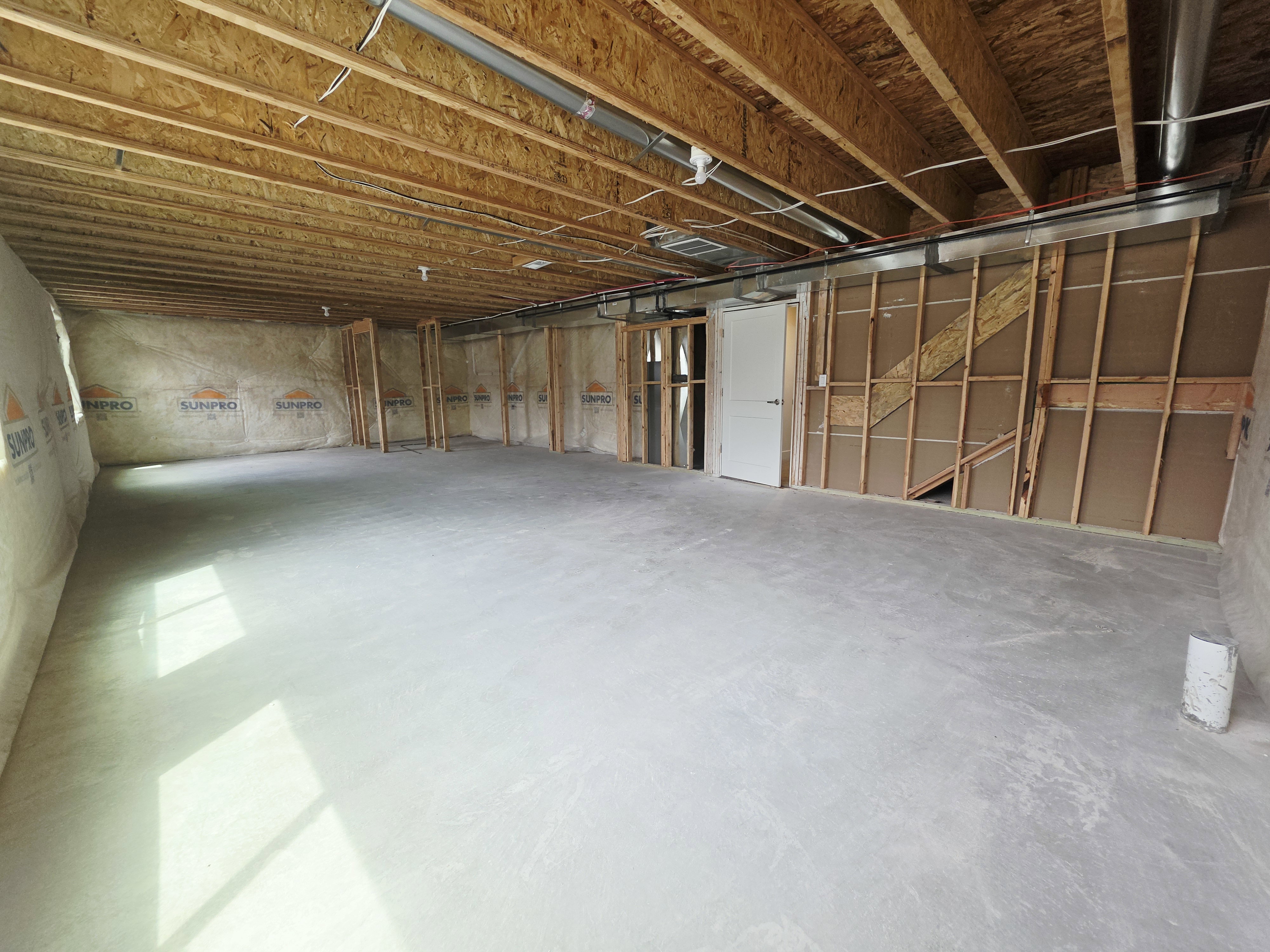 Unfinished basement featuring a concrete floor, exposed wood ceiling joists, and framed walls