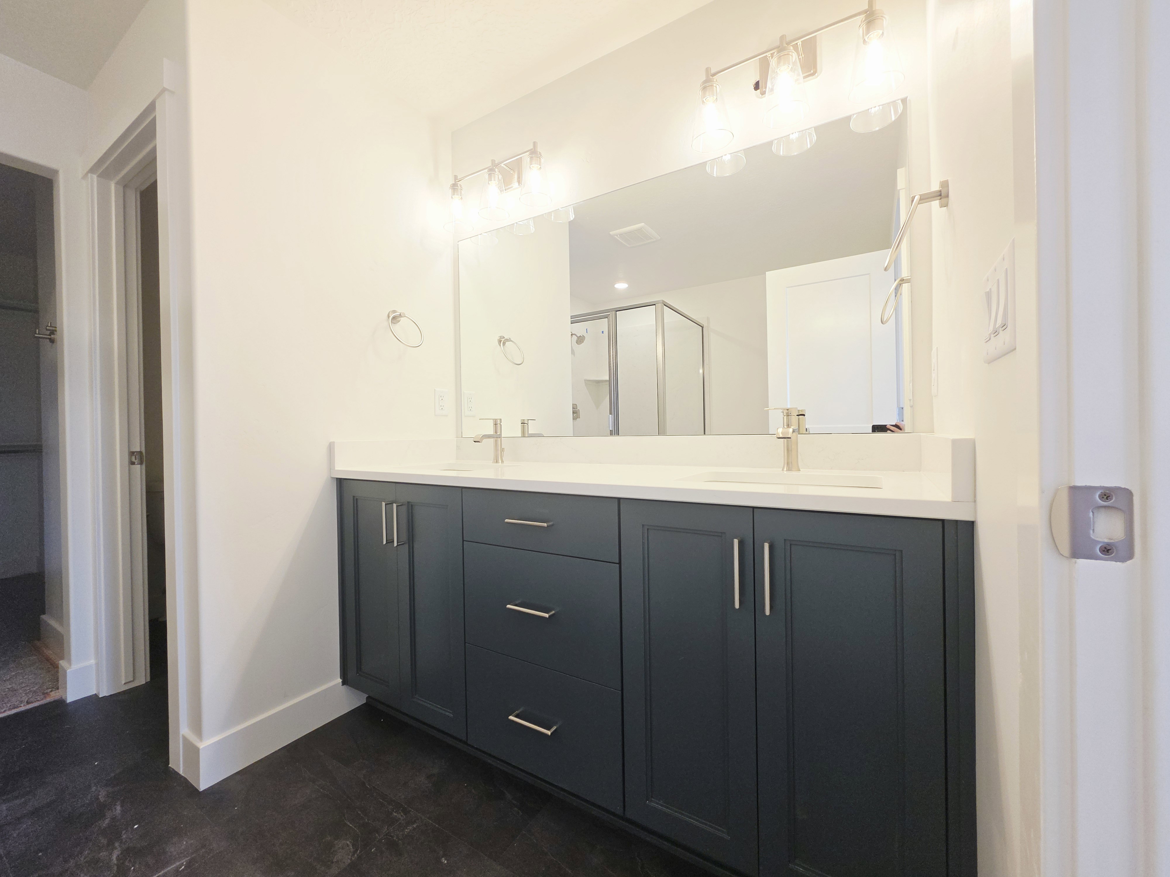 Dual vanity with dark cabinetry, integrated sinks, brushed nickel fixtures, and a glass-enclosed shower visible in the reflection