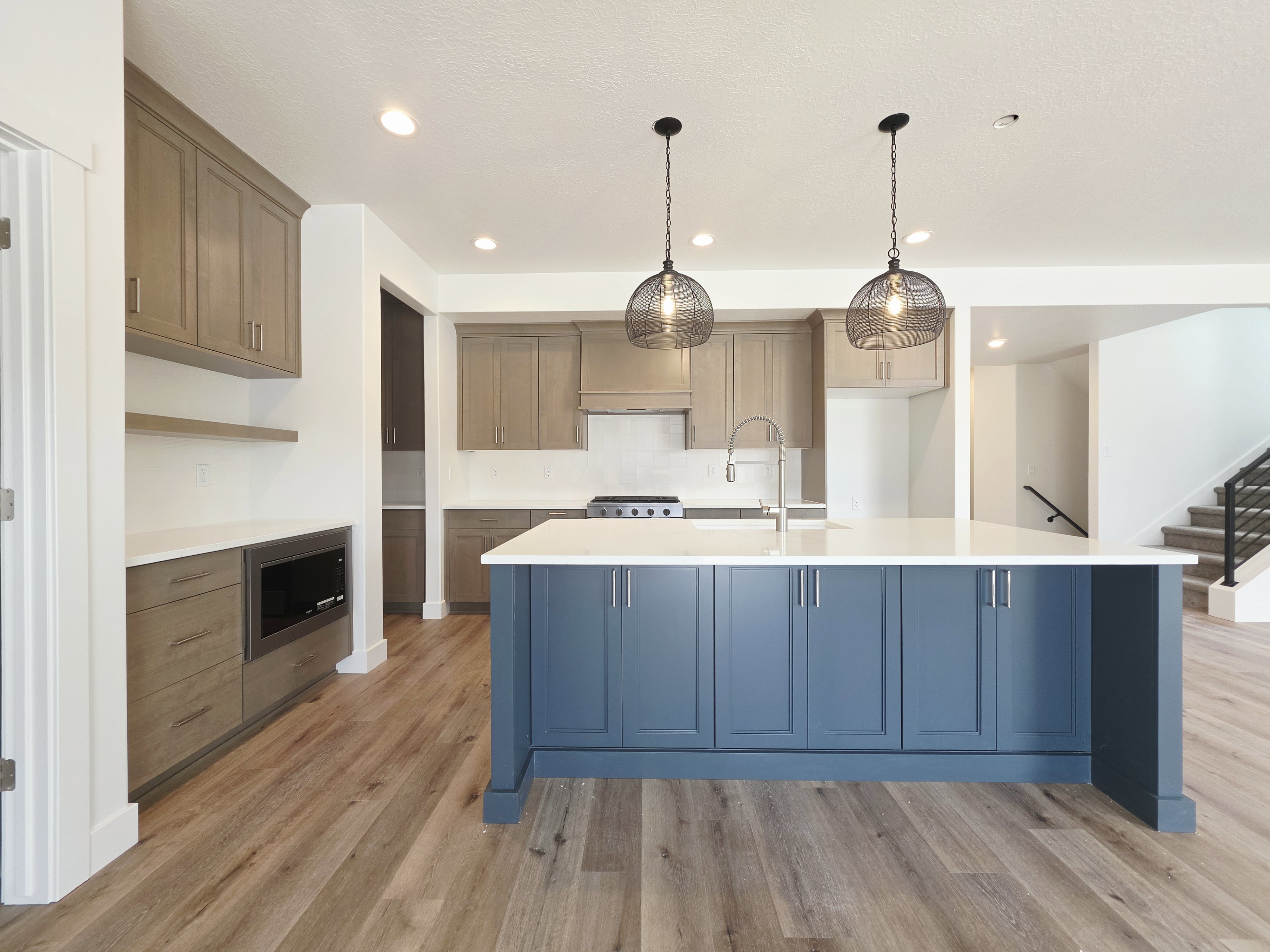 Open-concept kitchen featuring a large island with blue cabinetry, white countertops, stainless steel appliances, and wood-finish flooring