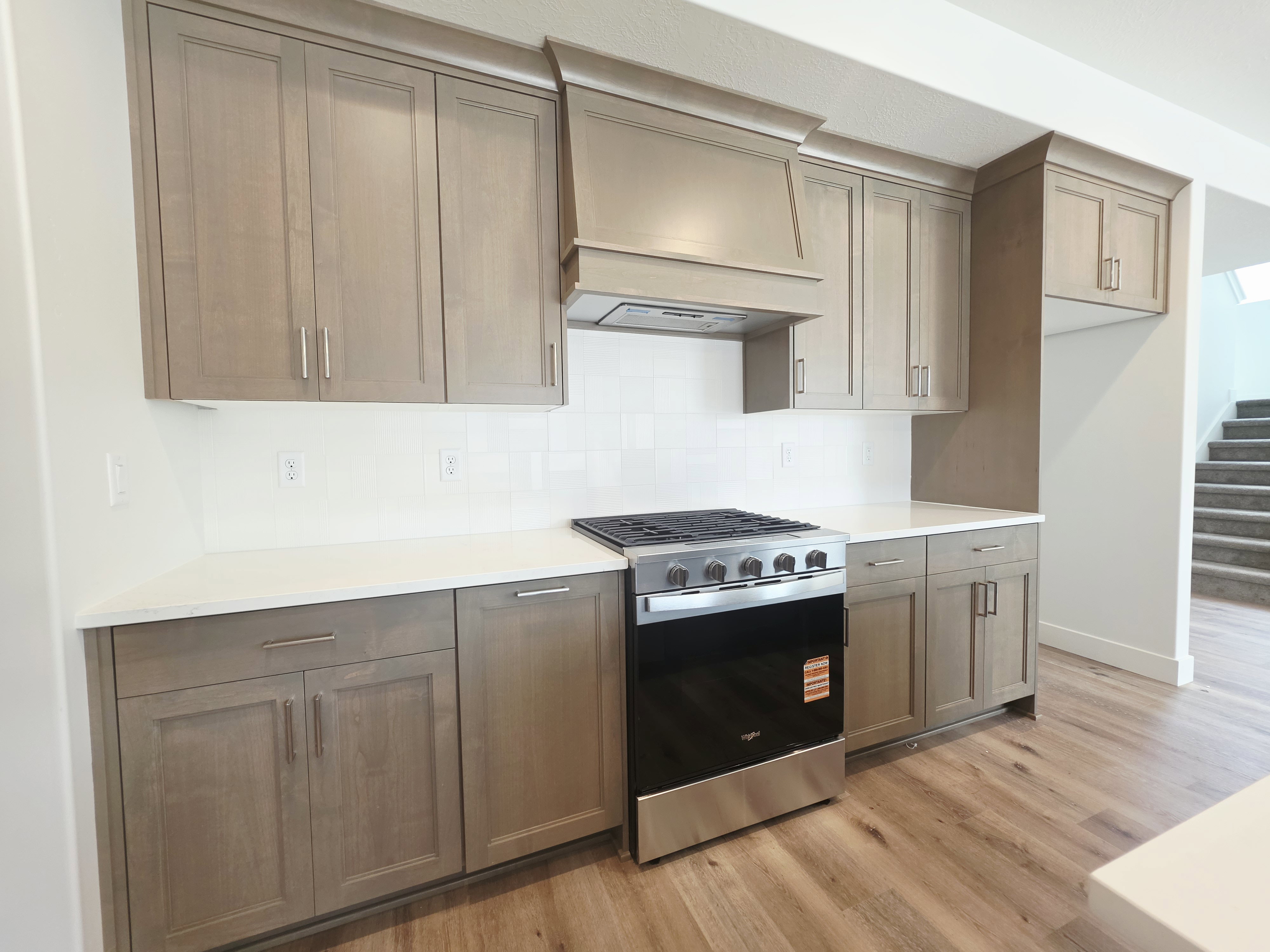 Kitchen featuring wood-finish flooring, white countertops, subway tile backsplash, stainless steel range, and light wood cabinetry with brushed nickel hardware