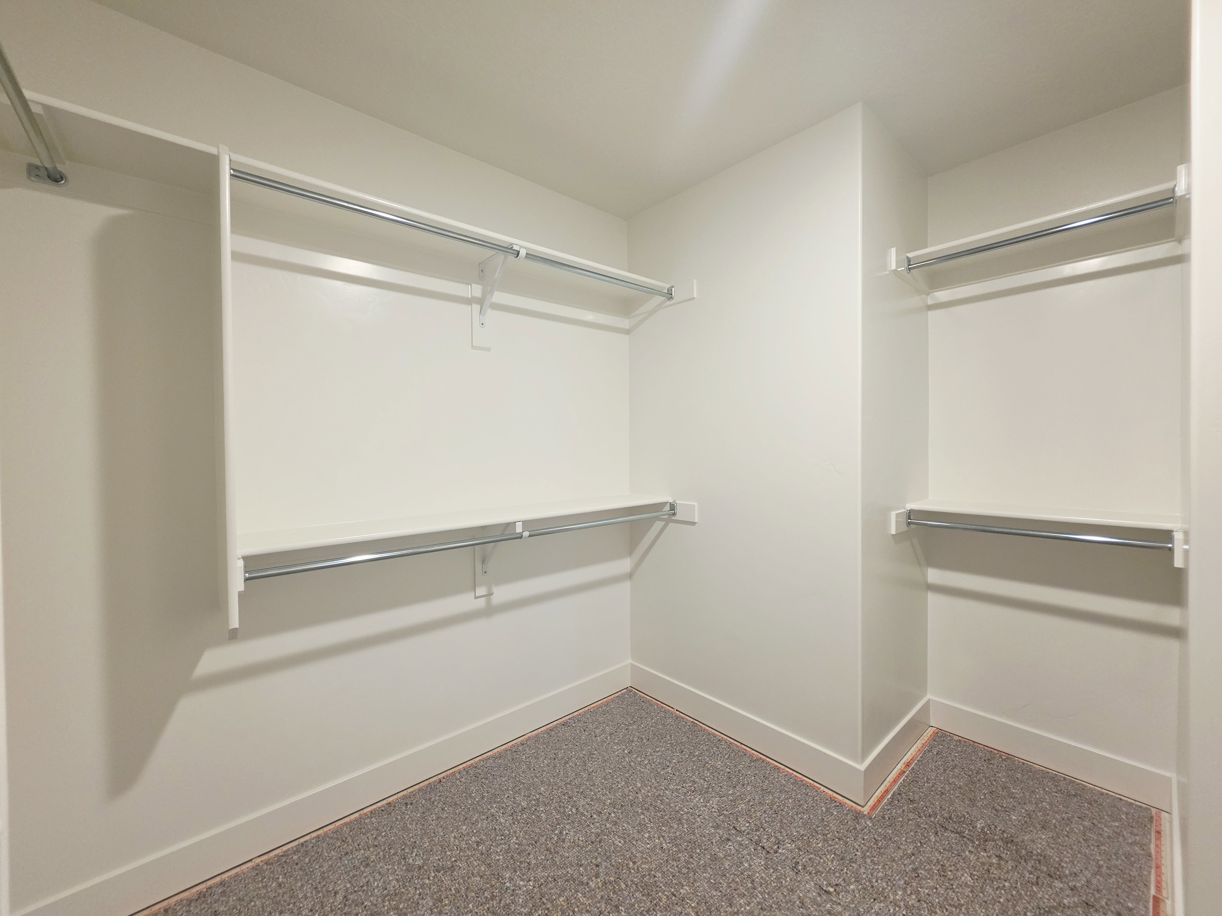 Walk-in closet featuring white painted walls and trim, multiple levels of shelving, chrome hanging rods, and gray carpet flooring