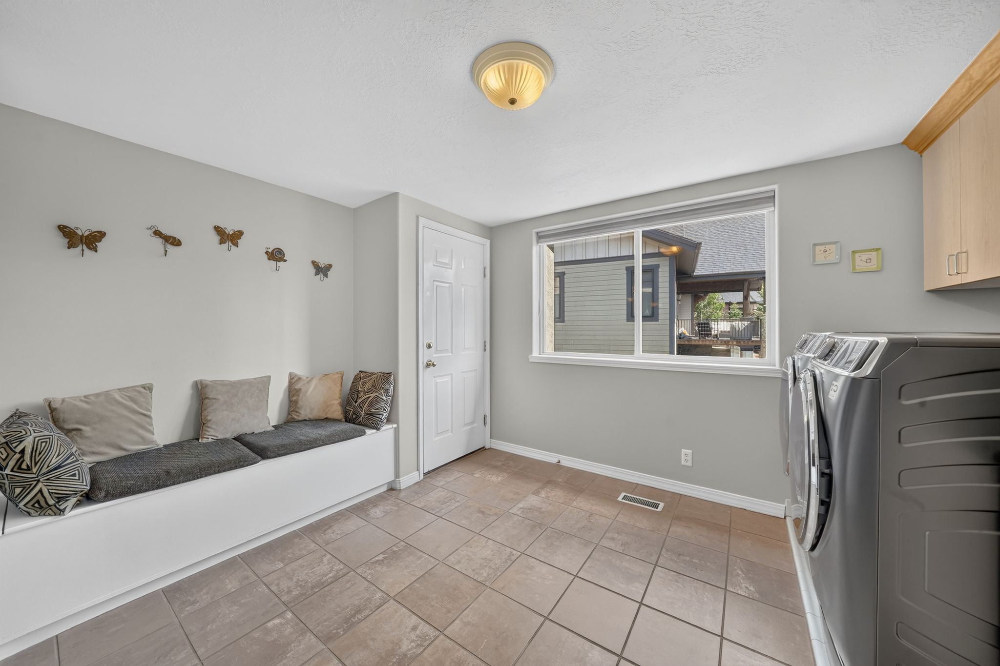Laundry area featuring tiled flooring, a built-in storage bench, and natural wood-finish cabinetry
