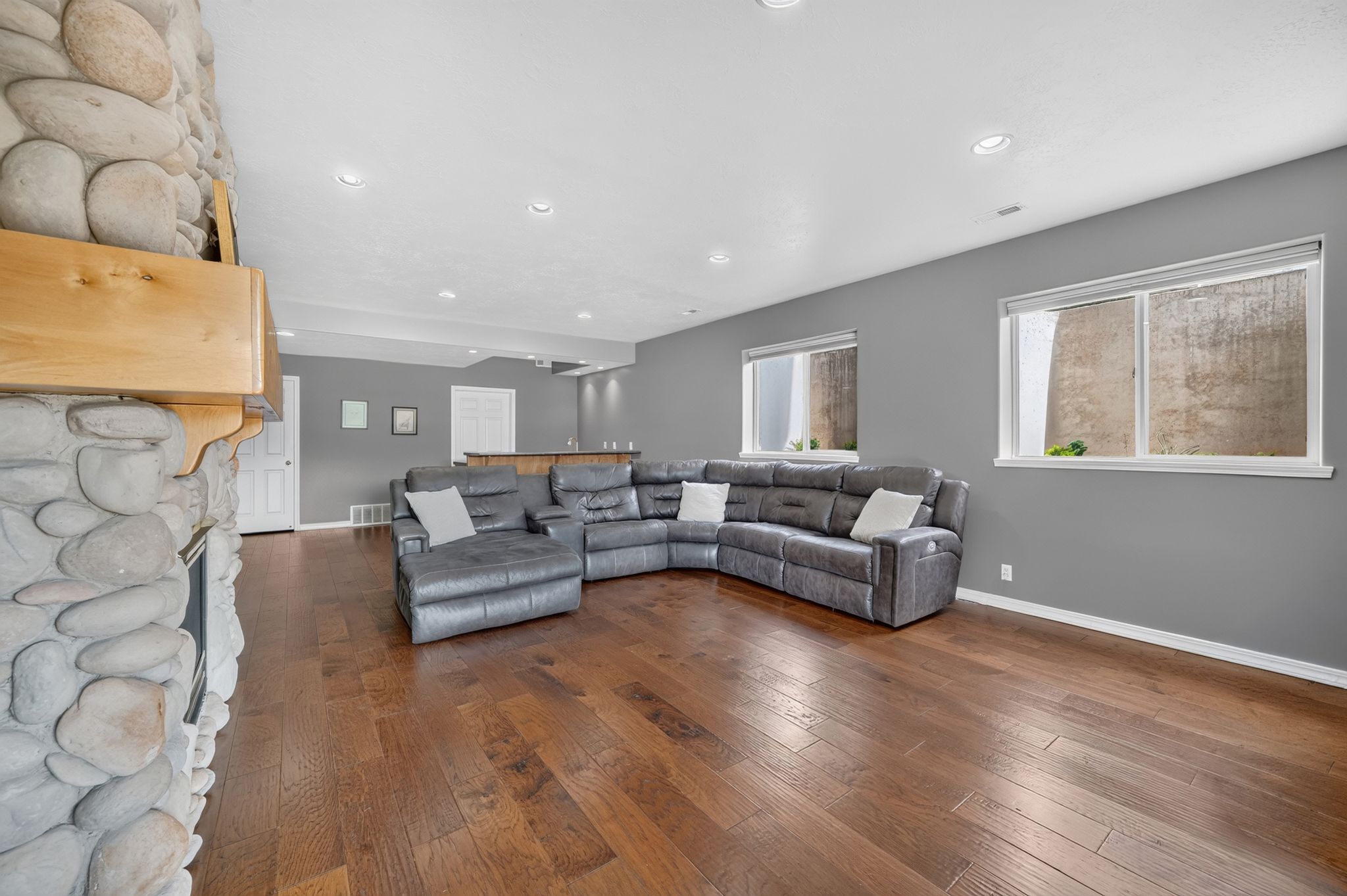 Spacious entertainment area featuring wood-finish flooring, a stone-faced fireplace with a wood mantel, recessed lighting, and a built-in bar with wood countertops