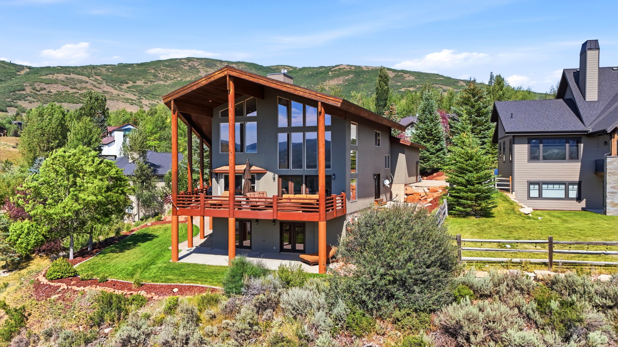 Contemporary architectural style featuring expansive glazing, a multi-level deck with wooden railings, and a prominent pitched roofline
