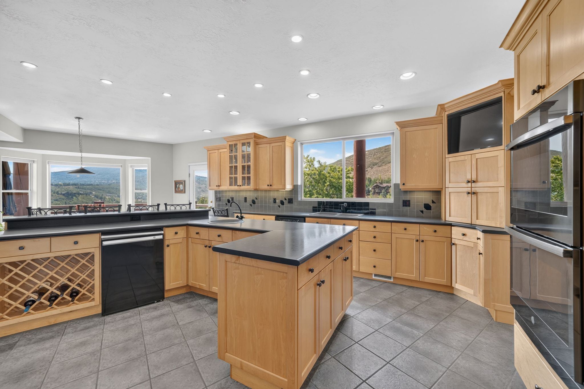 Kitchen featuring a central island, light wood cabinetry, black countertops, and grey tile flooring