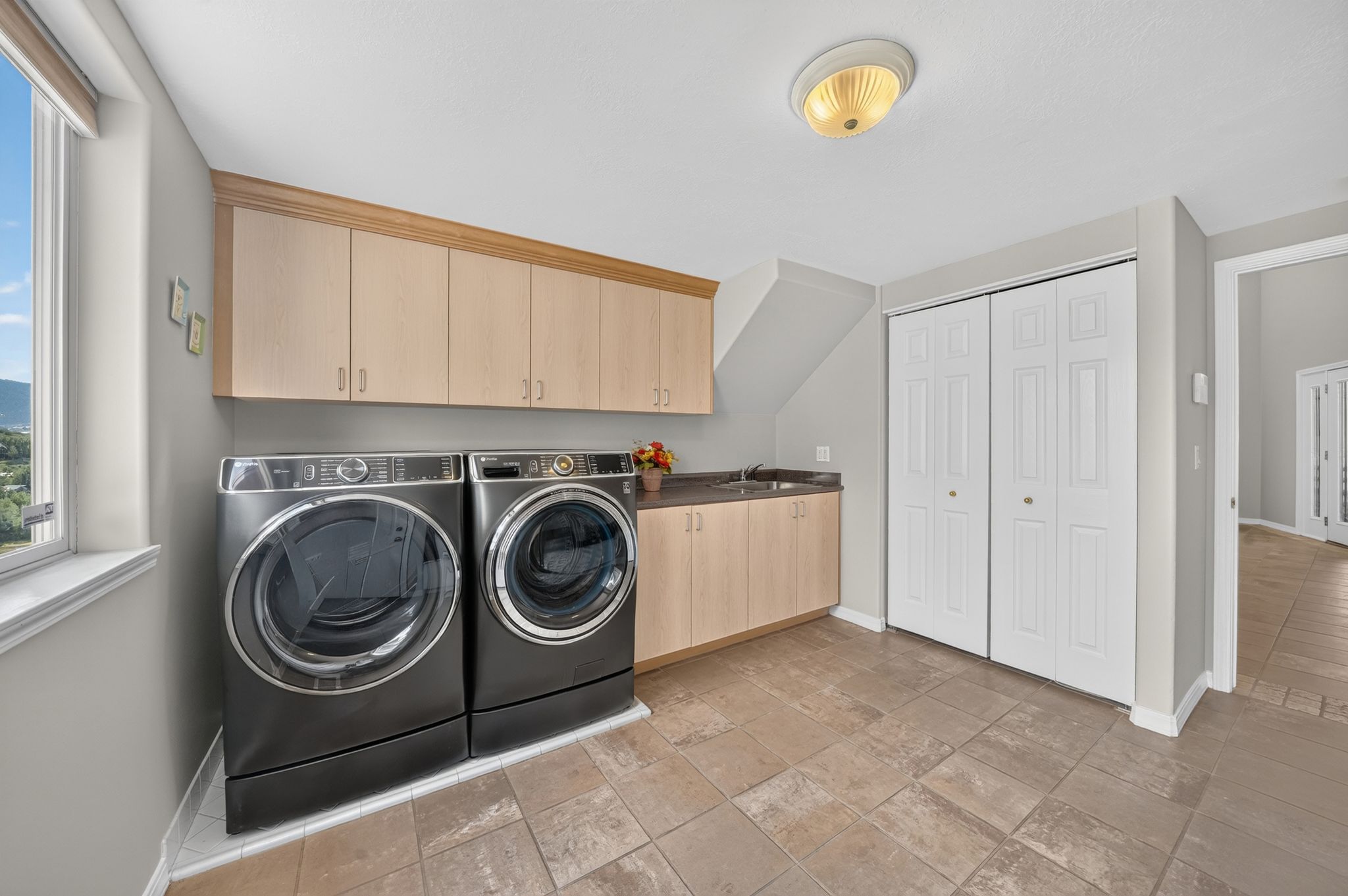Laundry room featuring light wood cabinetry, a utility sink, and durable tile flooring