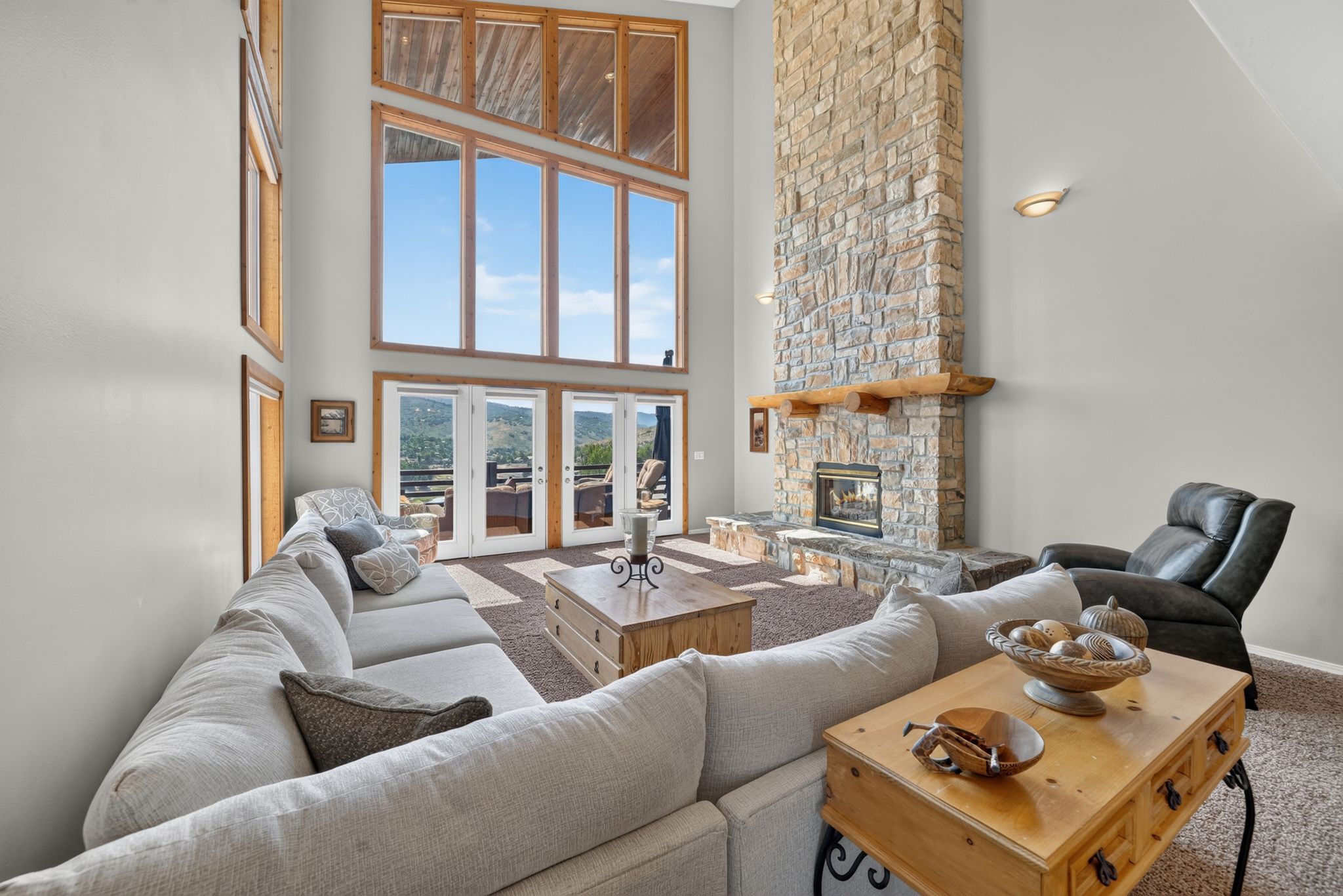 Great room featuring a floor-to-ceiling stone fireplace, large picture windows, and double French doors opening to an exterior balcony