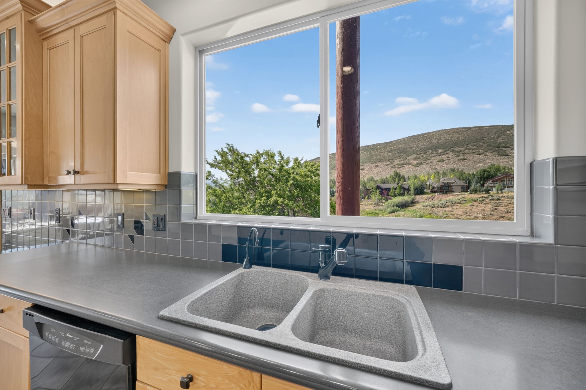 Kitchen workspace featuring light wood cabinetry, a dual basin sink, and a black dishwasher