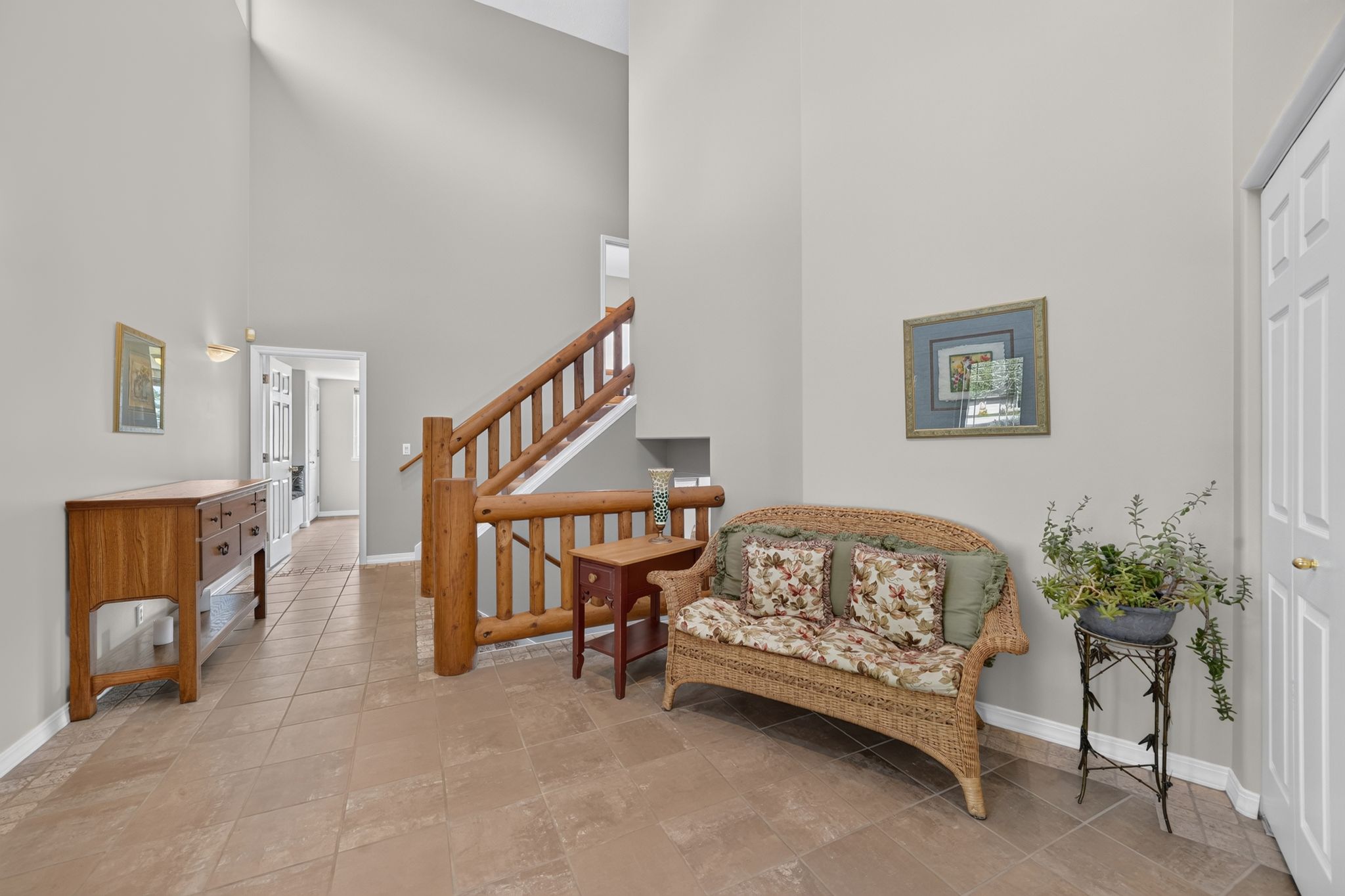 Two-story entryway featuring light gray walls, large format tile flooring, and a log-style staircase with wooden railings
