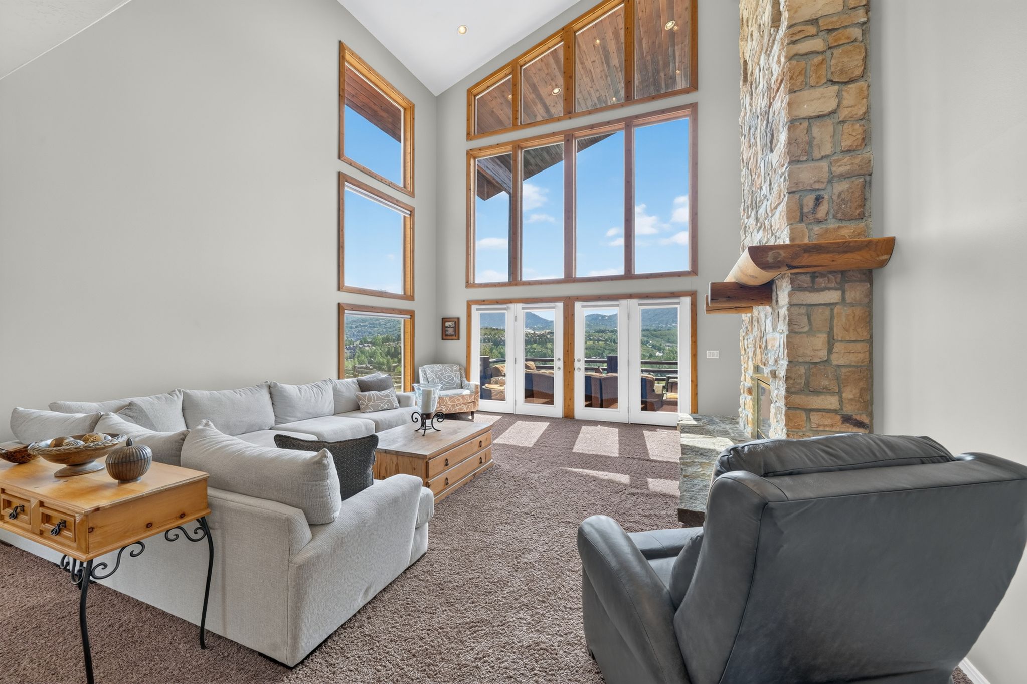 Great room featuring a vaulted ceiling with exposed wood beams, a floor-to-ceiling stone fireplace with a wood mantle, and expansive windows offering distant landscape panoramas