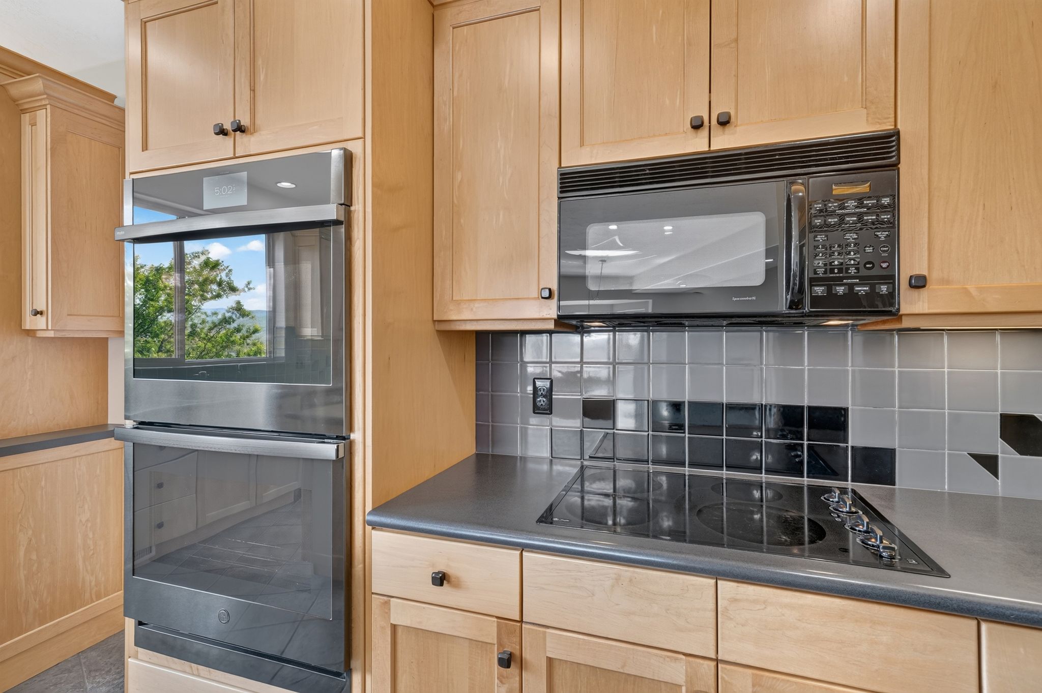 Kitchen featuring light wood cabinetry with dark hardware, a built-in stainless steel double oven, and a black microwave