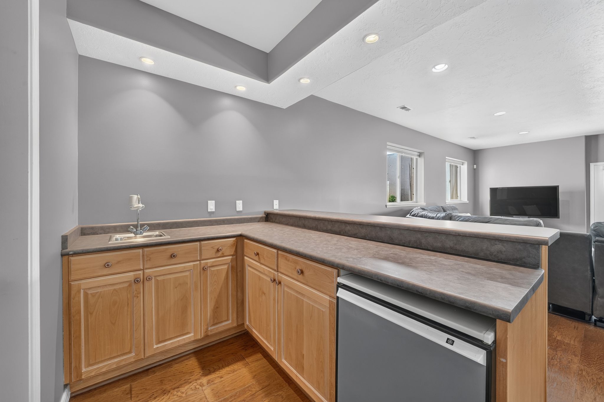 Entertainment area featuring a built-in wet bar with a stainless steel sink, light wood cabinetry, and a compact refrigerator