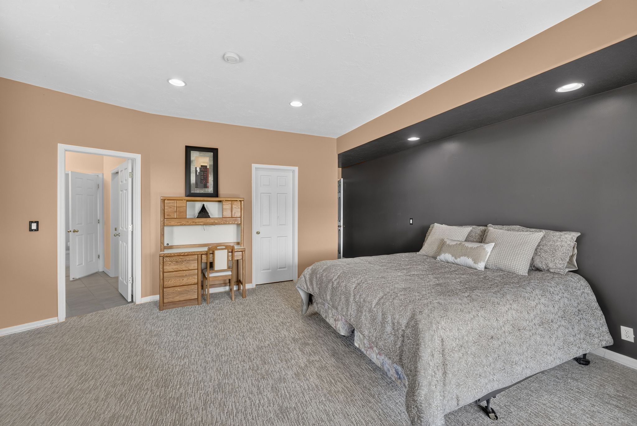 Carpeted interior space featuring a recessed ceiling, overhead lighting, a built-in architectural soffit with integrated lighting, and multiple interior doorways