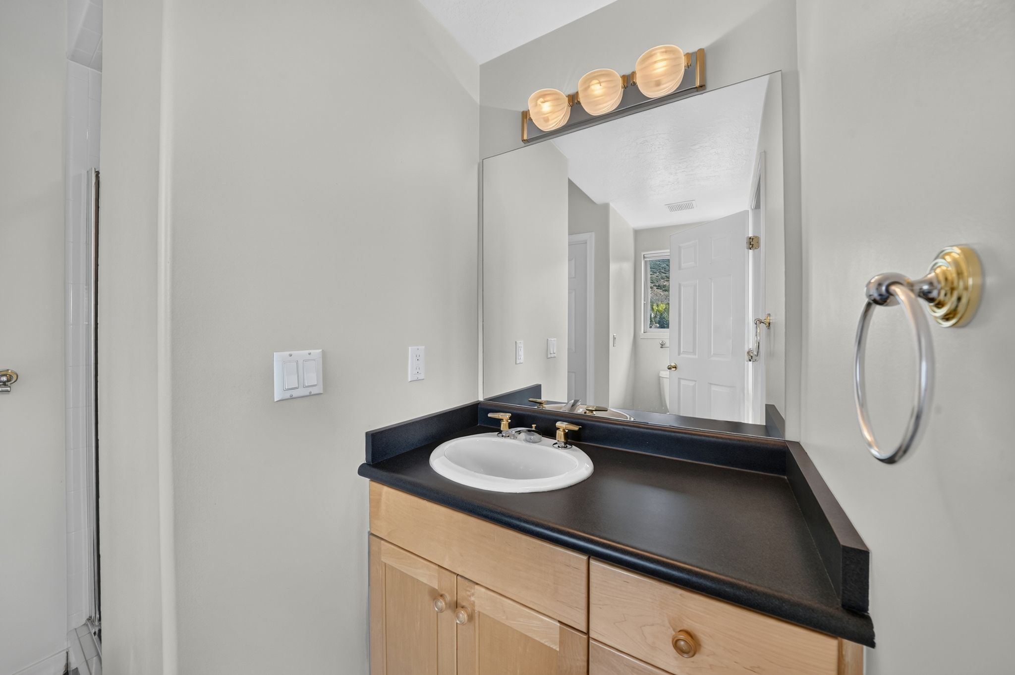 Bathroom vanity featuring a built-in sink, dark countertop, and light wood cabinetry