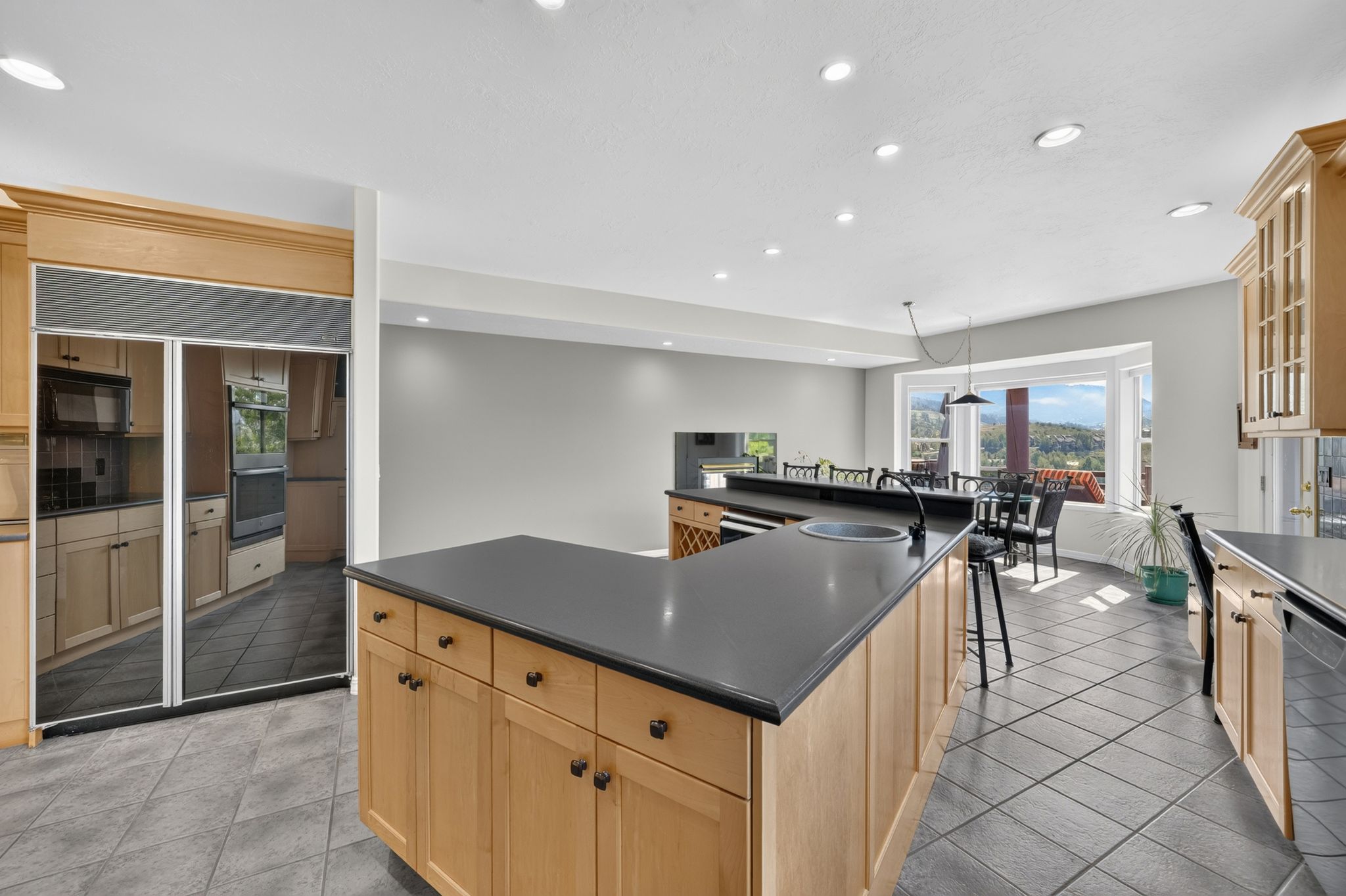 Kitchen featuring light wood cabinetry, black countertops, a built-in refrigerator, and tile flooring