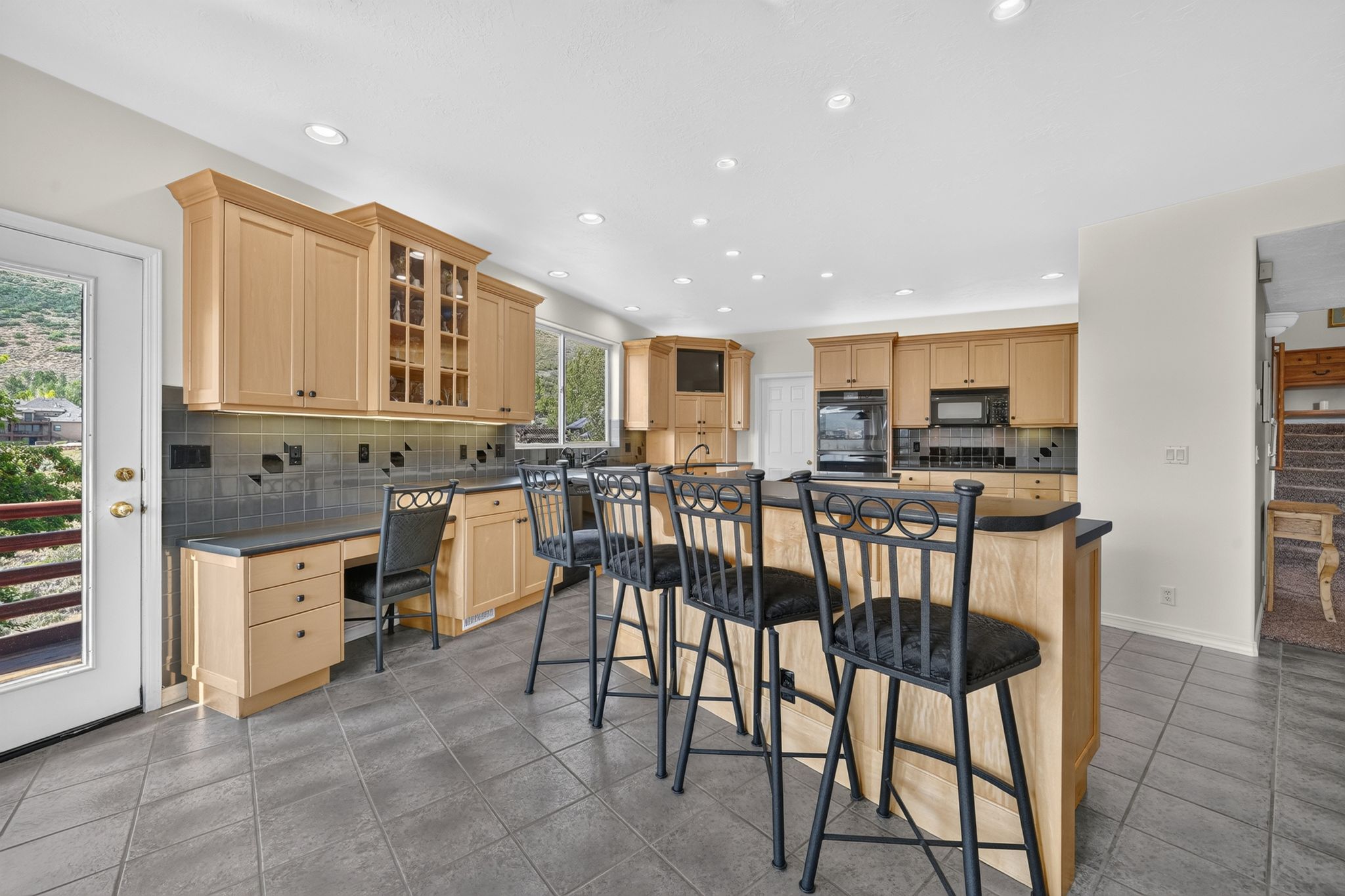 Kitchen featuring light wood cabinetry, a central island with bar seating, gray tile flooring, a built-in desk area, and recessed lighting
