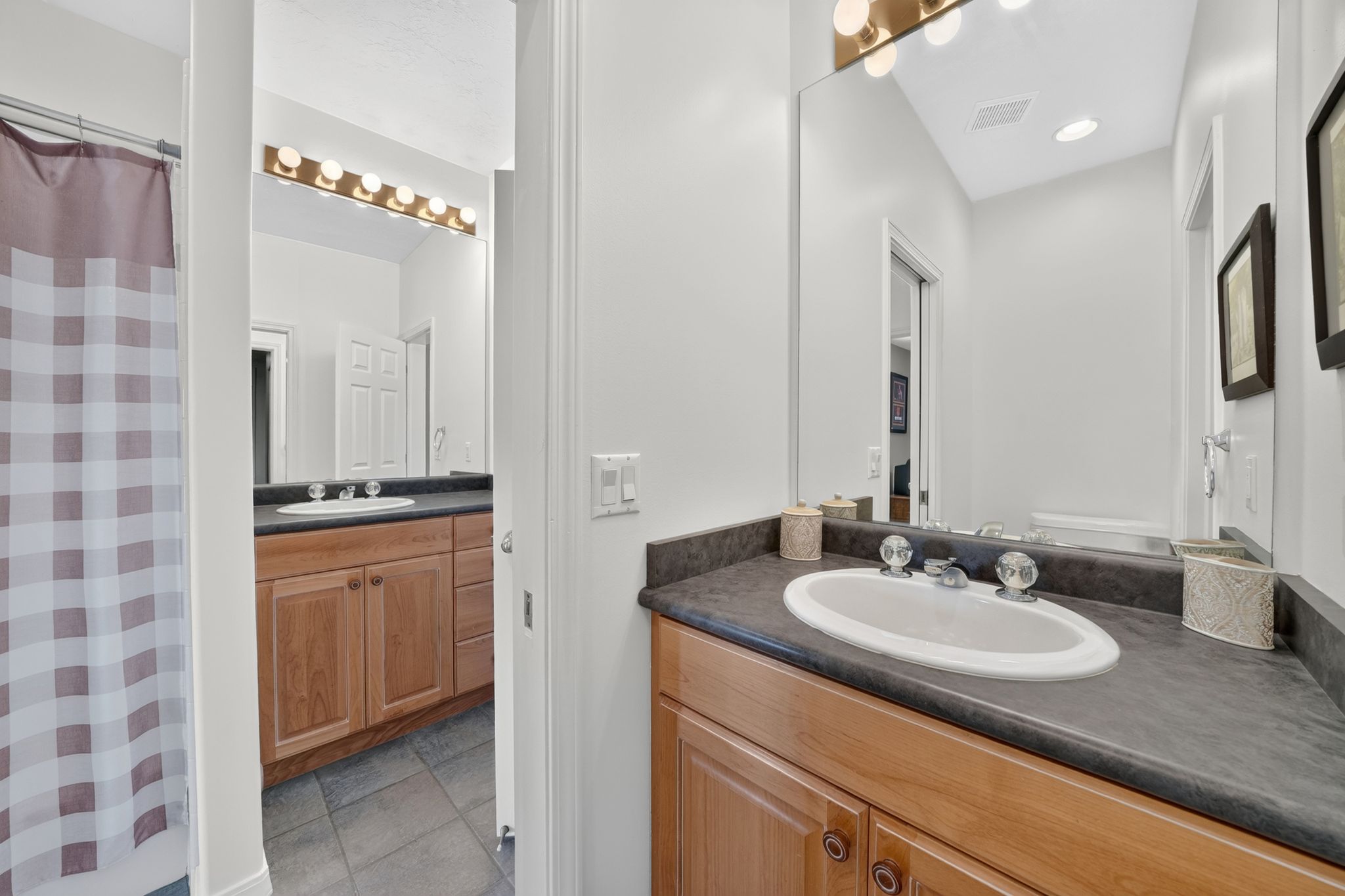 Bathroom vanity featuring a built-in oval sink, dark countertop, and light wood-finish cabinetry
