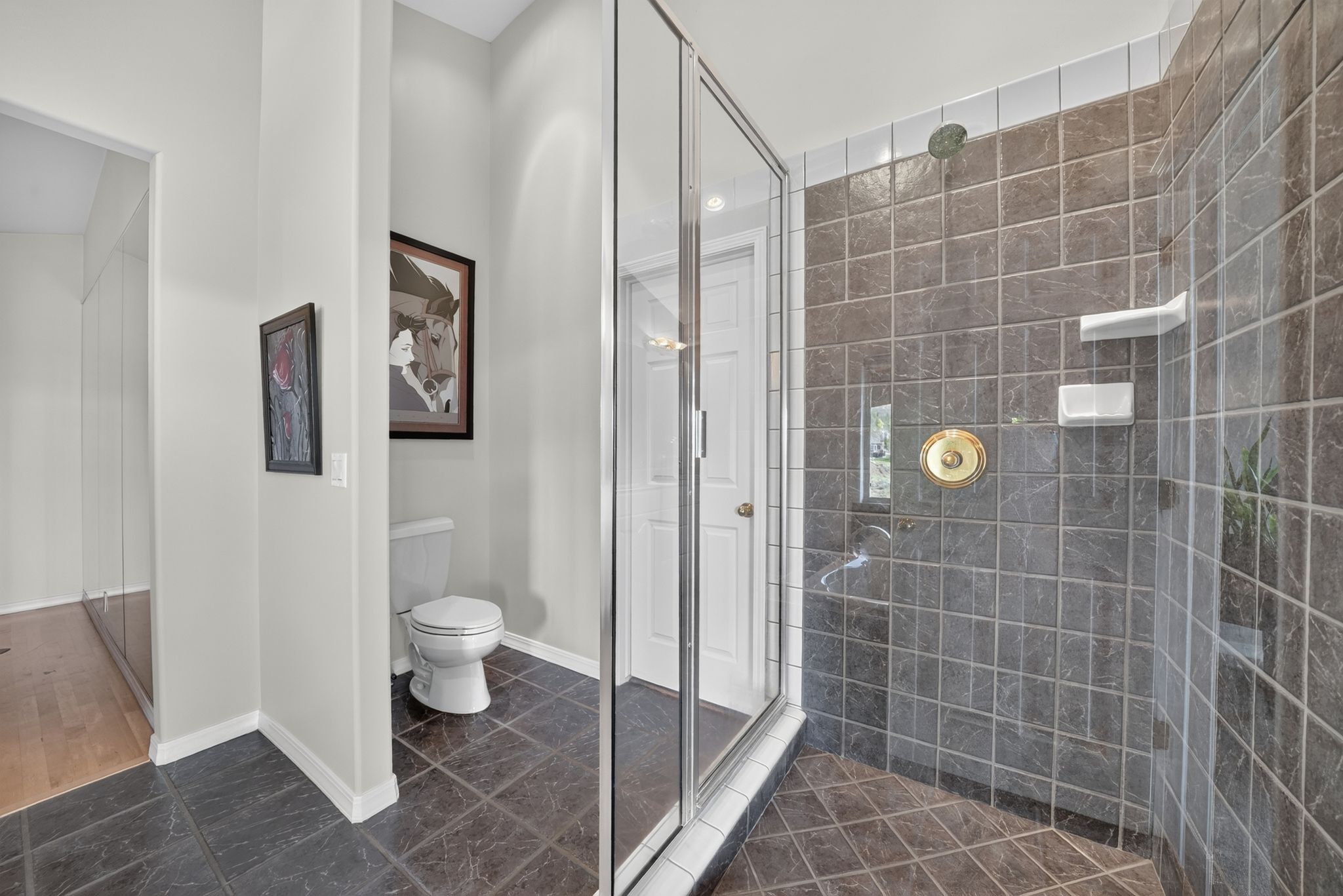 Shower enclosure featuring glass panels, square tile walls, and a brass shower control