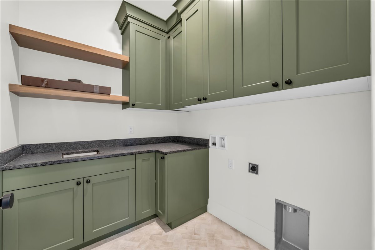 Laundry room featuring sage green cabinetry, dark speckled countertops, and wood-finish open shelving
