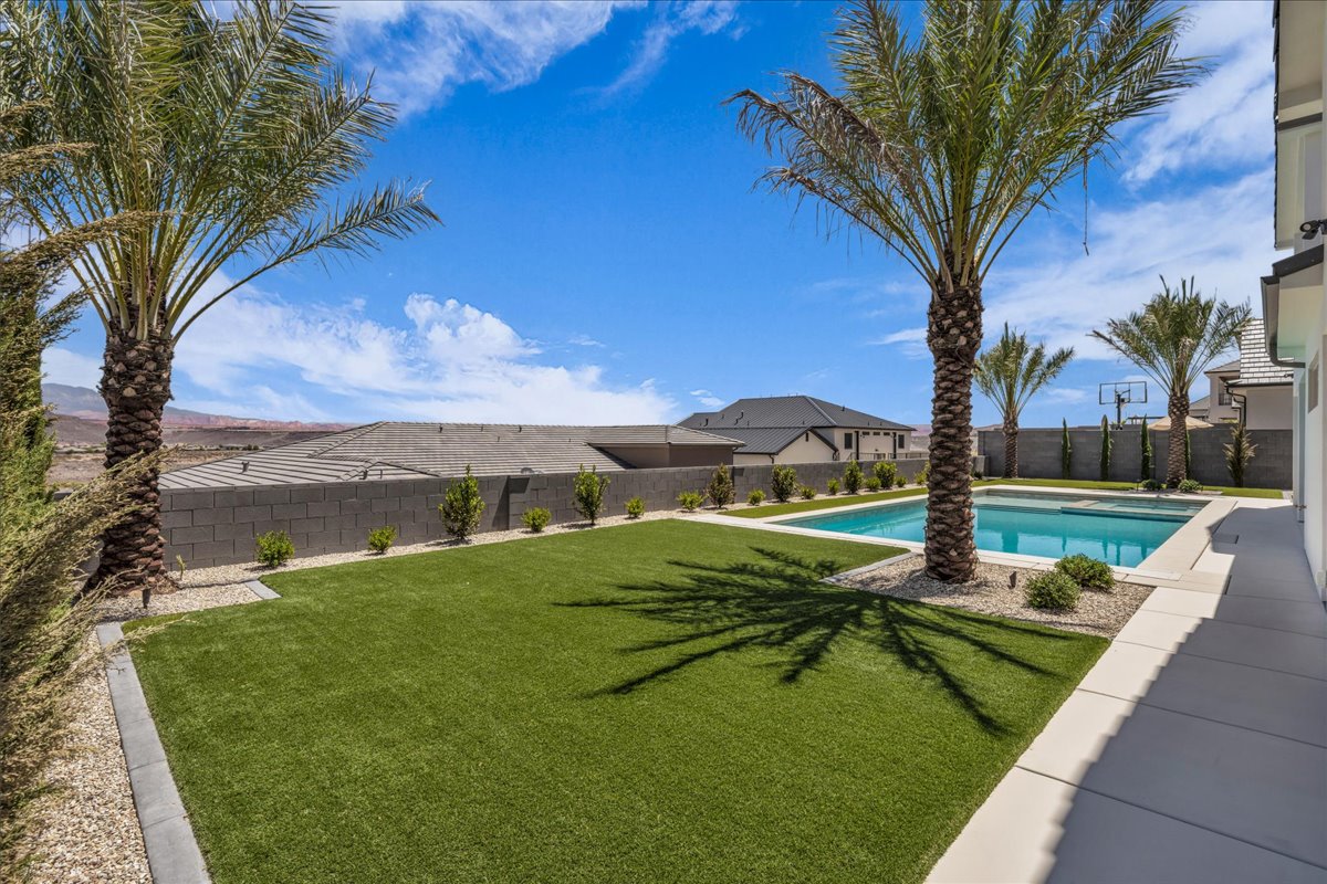 Expansive backyard featuring a rectangular swimming pool, artificial turf, perimeter block wall, and mature palm trees