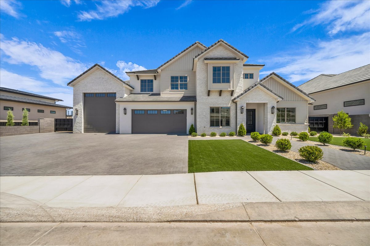 Modern farmhouse exterior featuring light-colored brick and vertical siding, a multi-car garage, manicured artificial turf, and a paved driveway