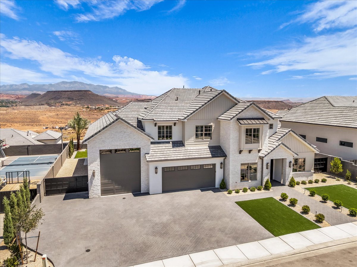 Expansive custom residence featuring a multi-car garage, manicured artificial turf landscaping, and a paver driveway