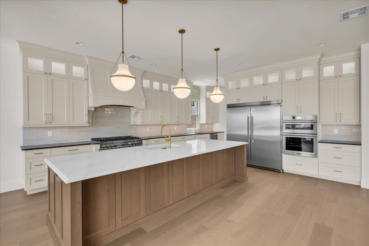 Gourmet kitchen featuring a large central island with a light wood-finish base and white countertop, stainless steel appliances, extensive white cabinetry with glass-front uppers, a gas range, and wood-finish flooring