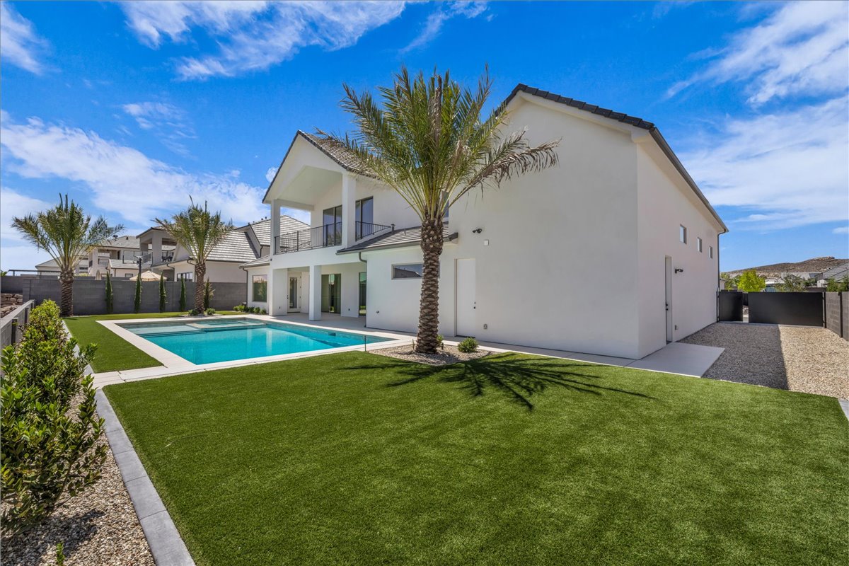 Expansive backyard featuring a rectangular swimming pool with surrounding hardscaping, a manicured artificial turf lawn, and mature palm trees