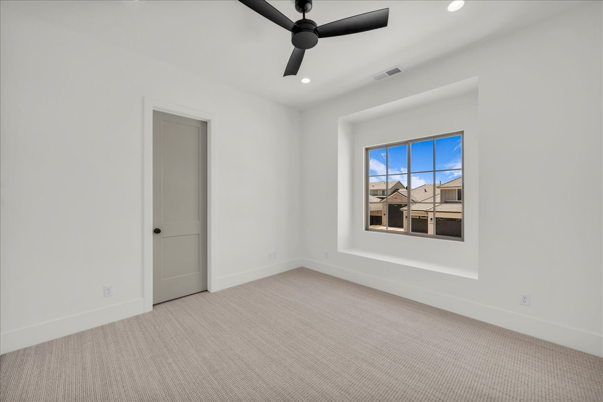 Crisp white walls define this room featuring textured carpeting, a recessed window with a deep sill, and a modern black ceiling fan with integrated lighting
