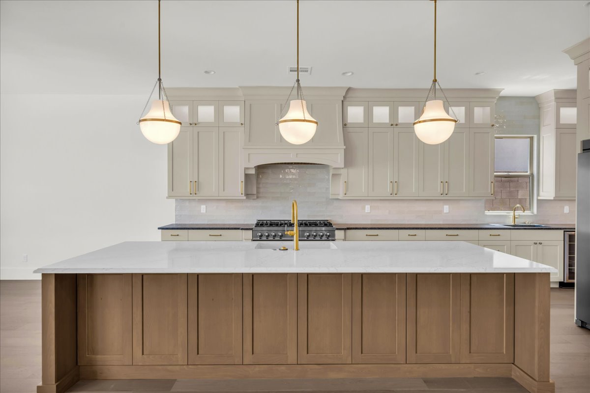 Kitchen featuring a large central island with a light-toned countertop, a gold-toned faucet, and three contemporary pendant lights