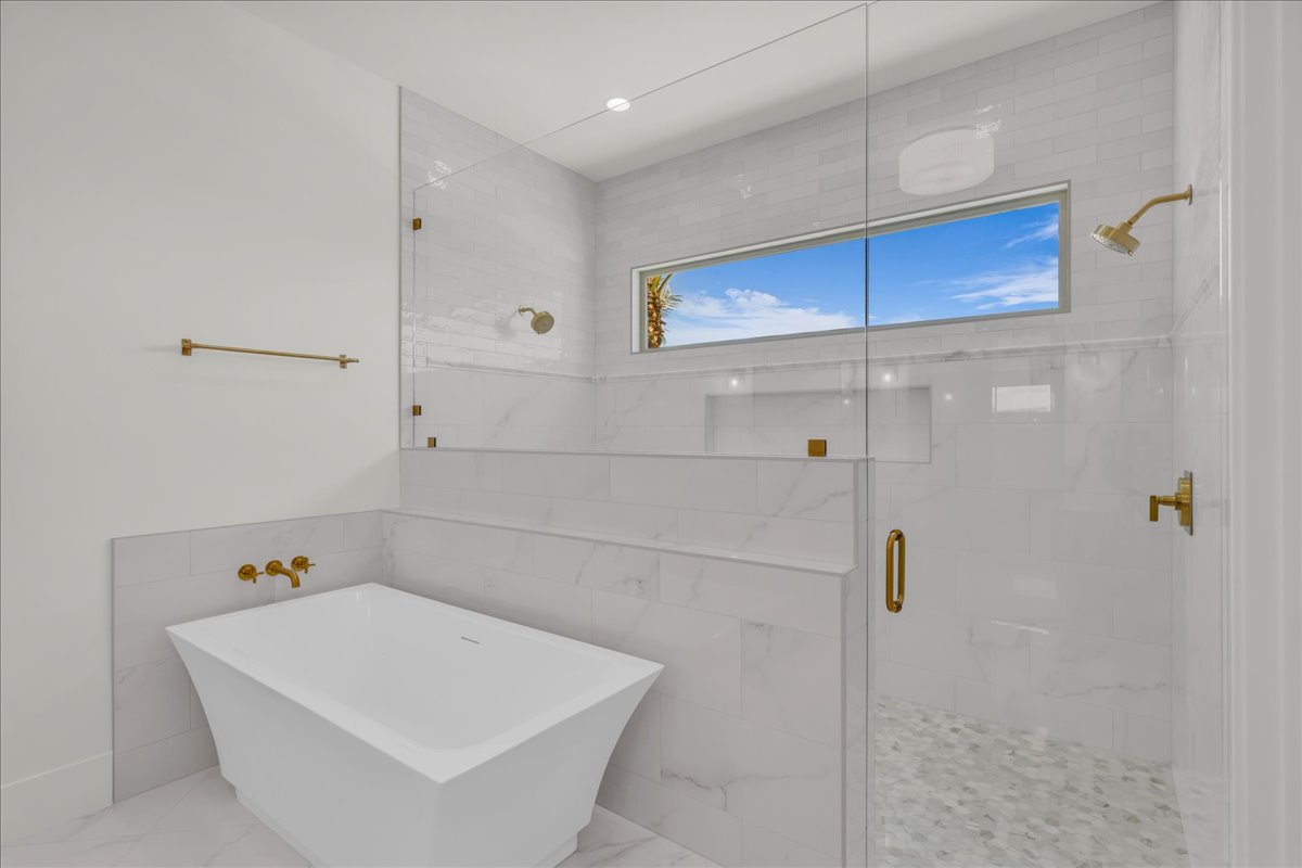 Bathroom featuring a freestanding tub, glass-enclosed shower with gold-tone fixtures, and patterned shower floor tiling