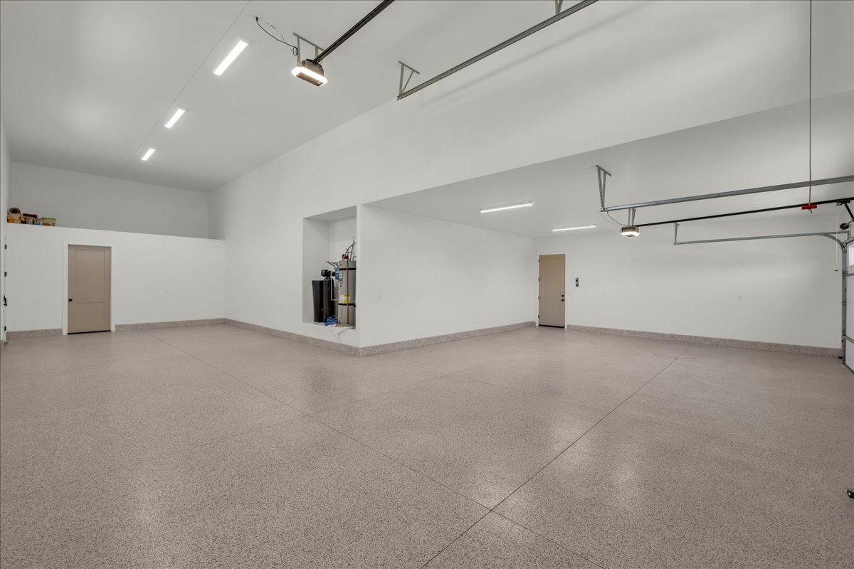 Spacious garage featuring a durable epoxy floor, high ceilings, multiple overhead LED light fixtures, and a dedicated storage loft