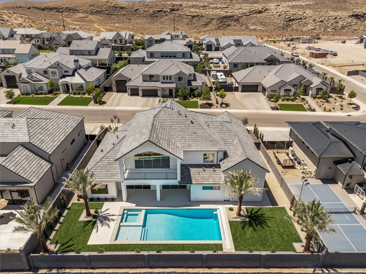 Modern residential property featuring a multi-level design, a private swimming pool with an integrated spa, an expansive turf lawn, mature palm trees, and a dedicated sports court