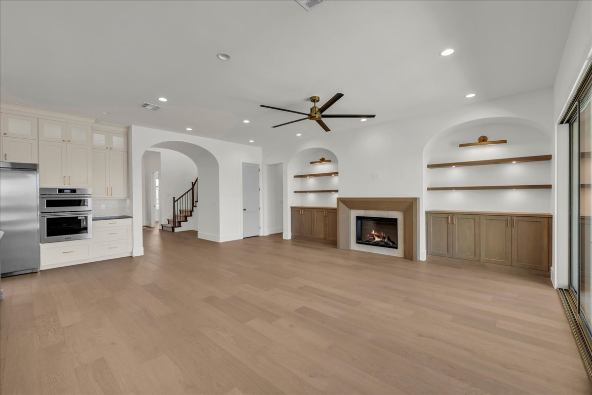Spacious living area featuring light wood-finish flooring, a contemporary fireplace, and built-in shelving with integrated lighting