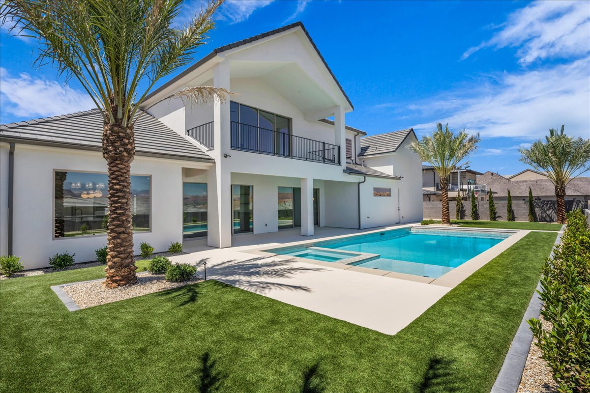 Expansive backyard featuring a rectangular pool with integrated spa, surrounded by a light-colored paved deck
