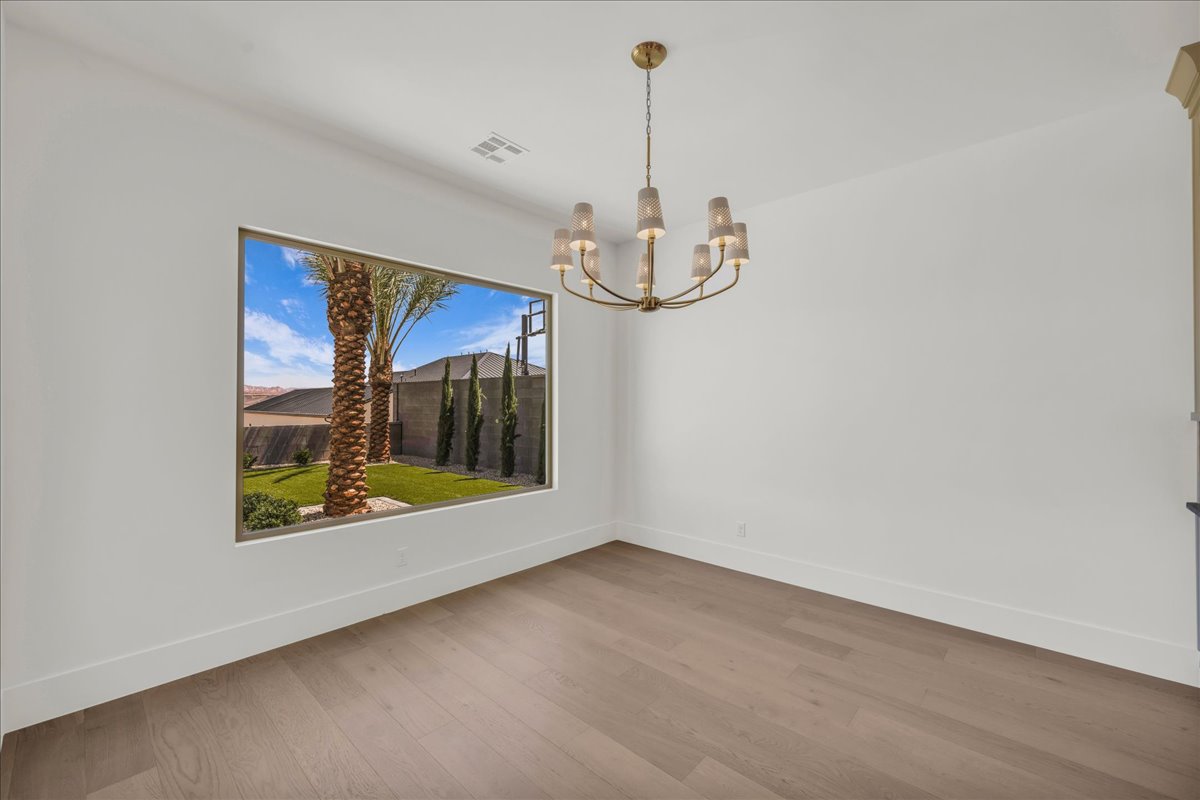 Spacious room featuring wood-finish flooring, a large picture window, and a contemporary brass chandelier